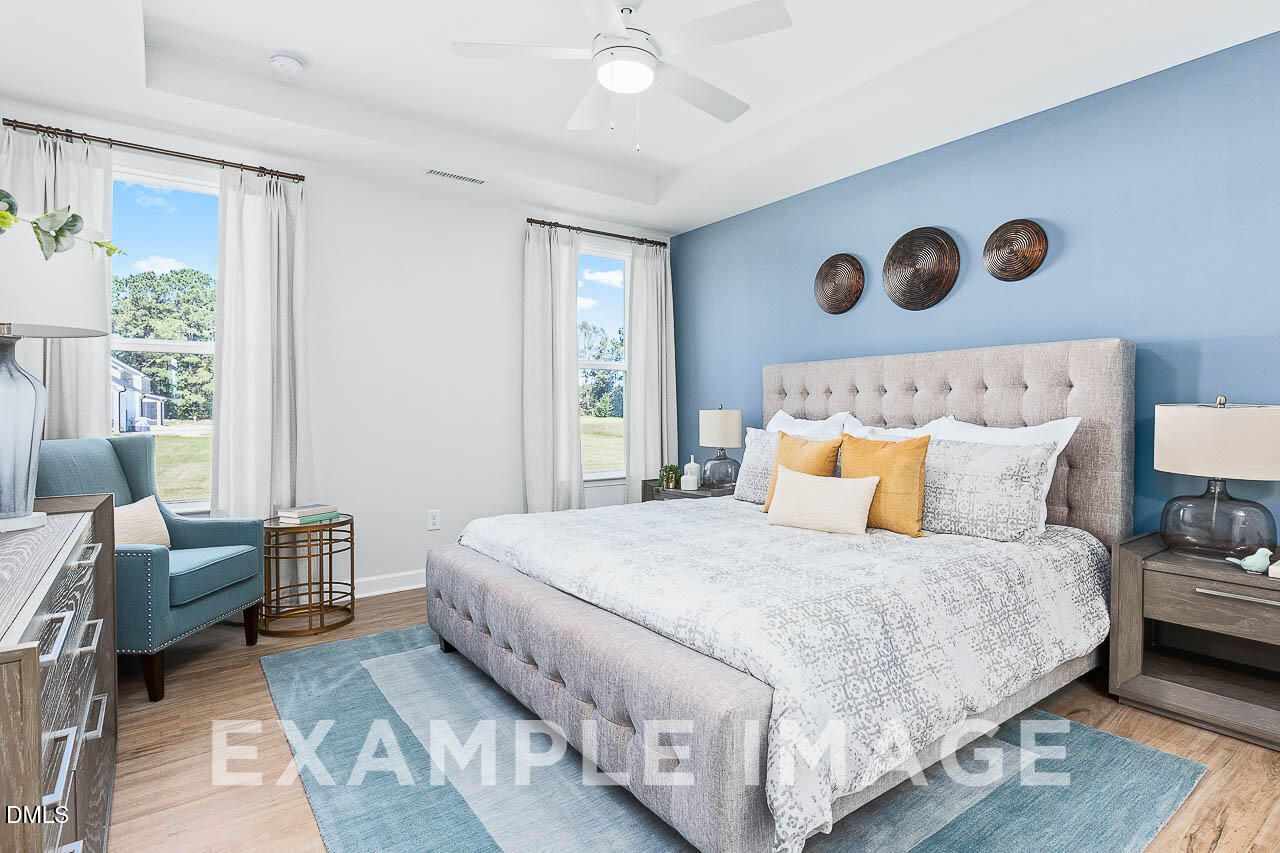 Serene master bedroom with tufted upholstered bed, blue accent wall, and natural light in Davidson Homes The Ash C, Lillington, NC