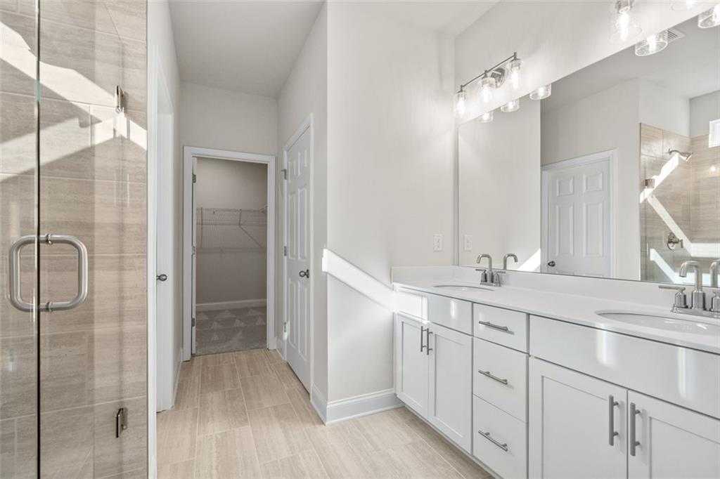 Modern master bathroom featuring double vanity, frameless glass shower, and white shaker cabinets in Davidson Homes The Ash C at Wehunt Meadows, Hoschton