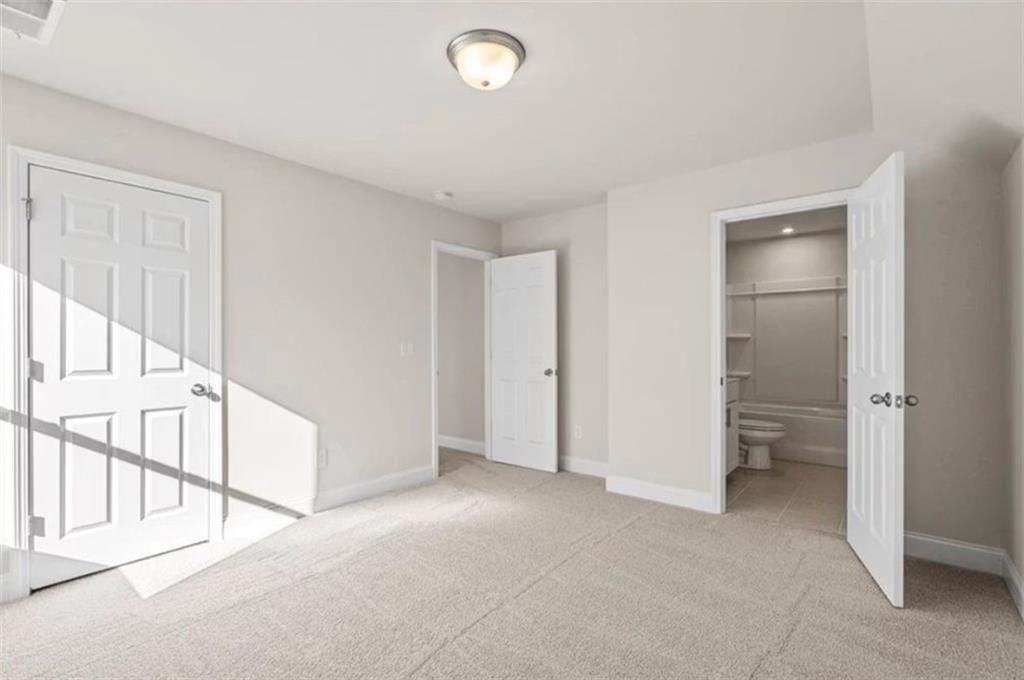 Bright bedroom with neutral carpet and en-suite bathroom in The Ash C floor plan at Wehunt Meadows, Hoschton, Georgia.