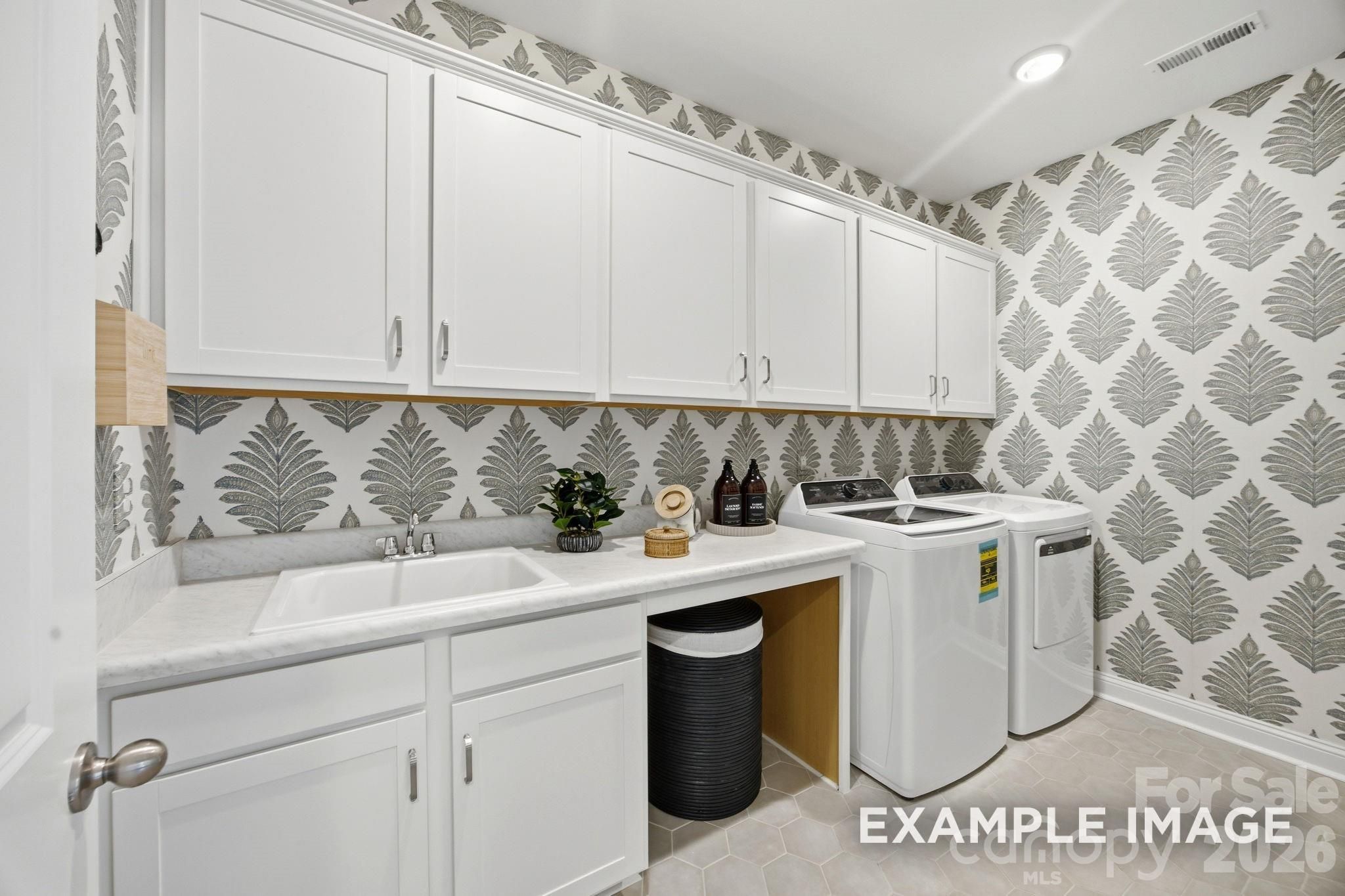 Laundry room with white cabinets, utility sink, and patterned wallpaper in The Hickory B II home at Windgate, Mooresville.