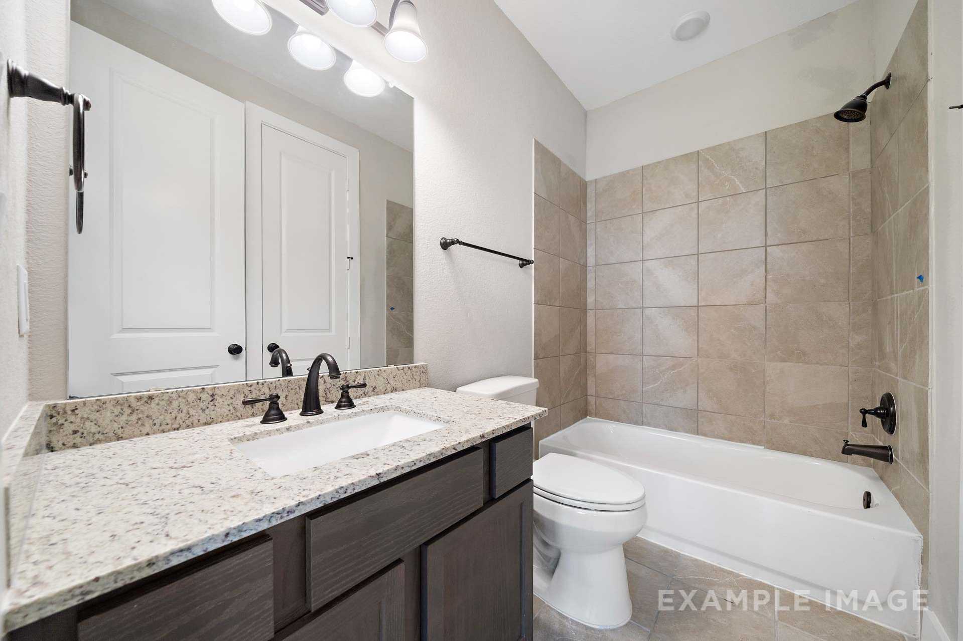 Master bathroom in The Elizabeth A with double granite vanity, dark wood cabinets, bathtub, toilet, and tiled shower walls