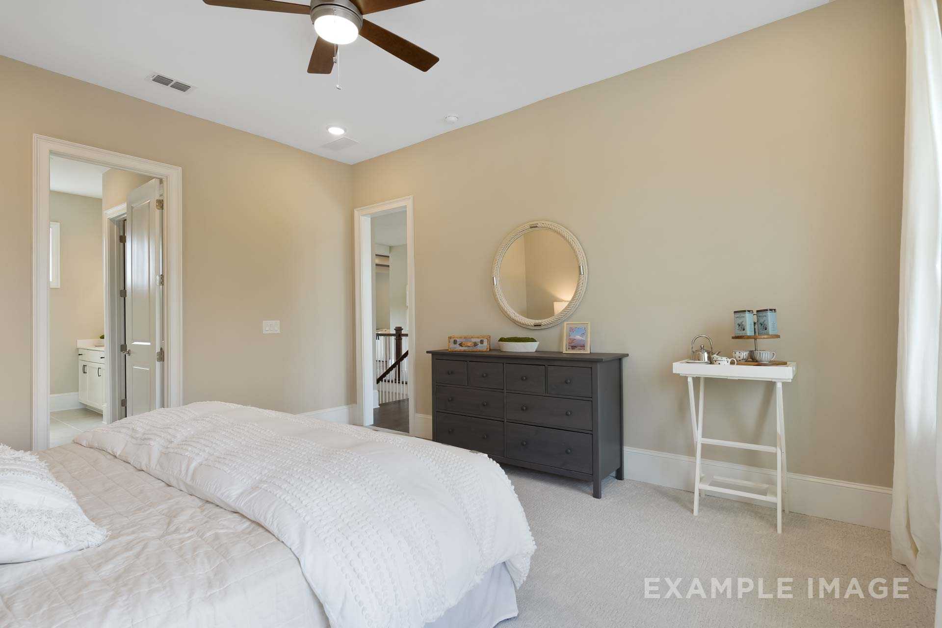 Spacious master bedroom in The Seaside with white king bed, dark dresser, round mirror, and en-suite bath door