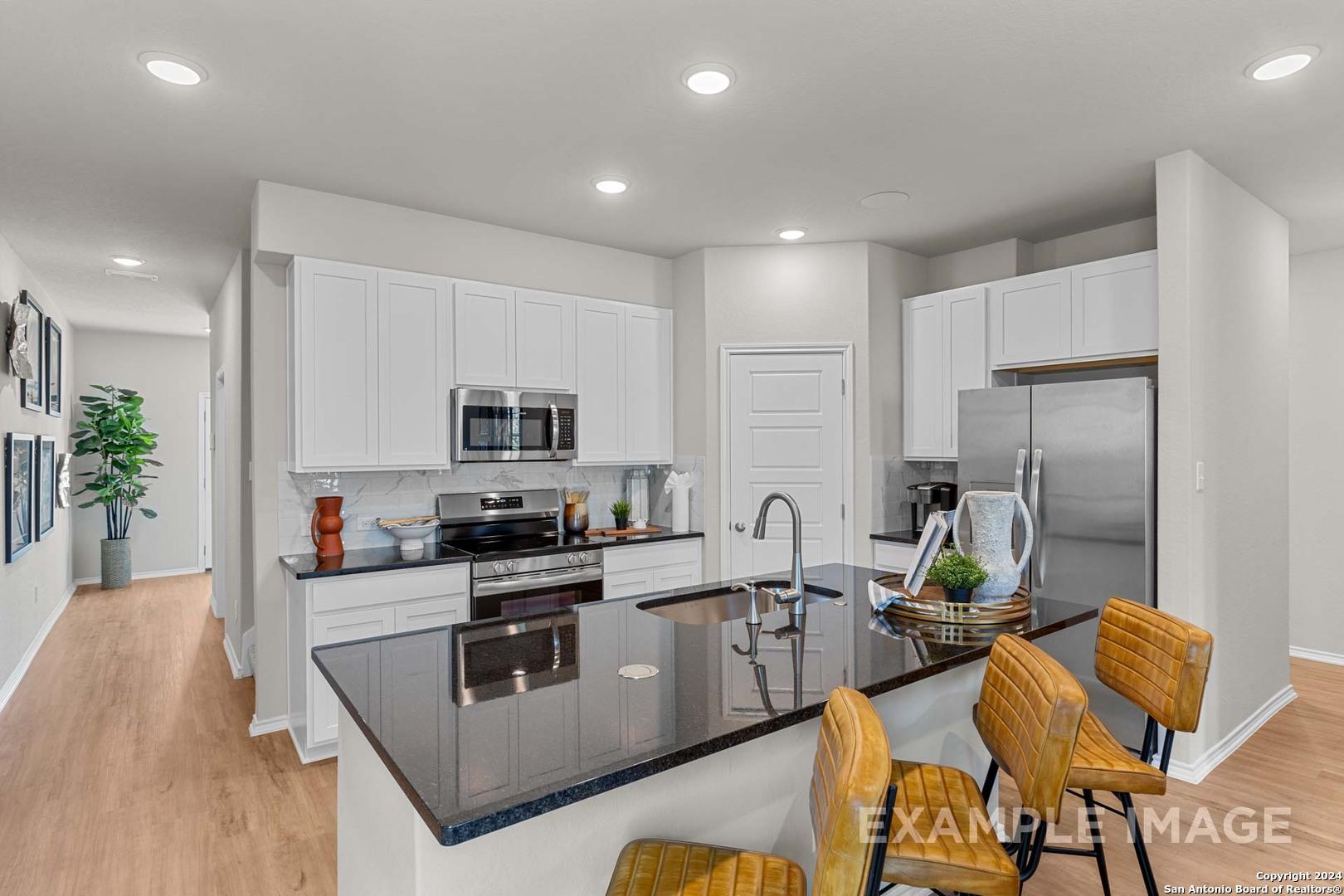 Modern kitchen with white cabinets, granite island, stainless appliances in The Sabine B 4-bedroom home, San Antonio, Texas