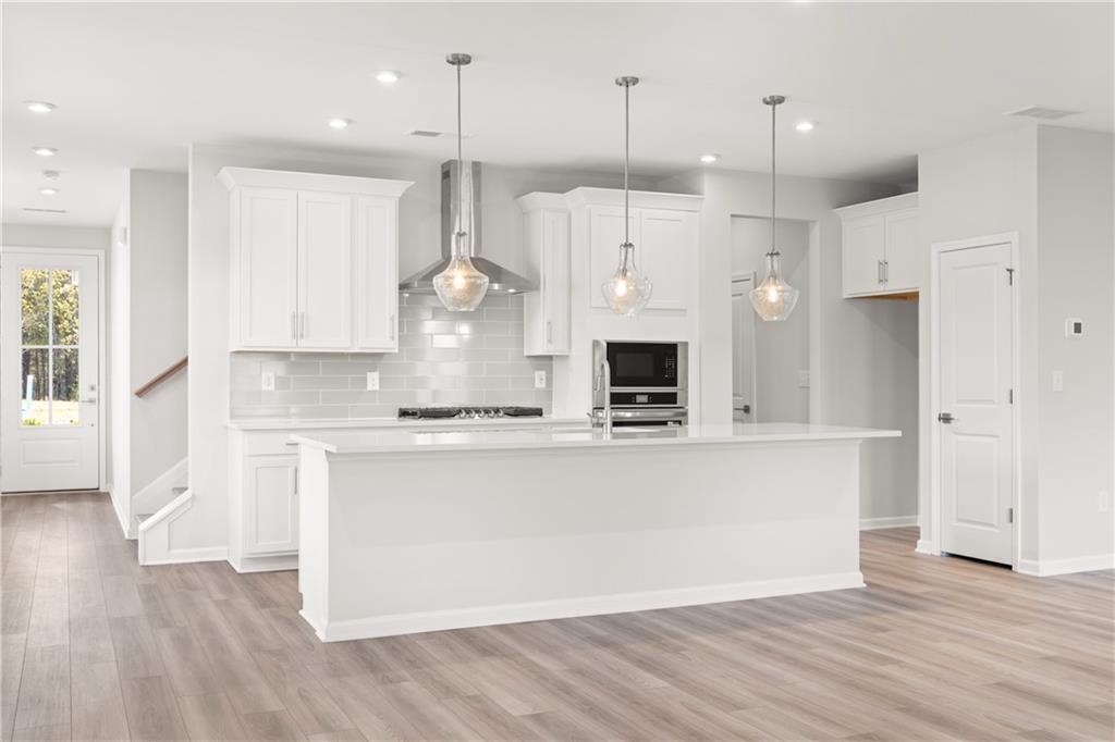 Modern white kitchen featuring stainless steel appliances, large island, subway tile backsplash, and pendant lights in The Cary A, Winder, GA