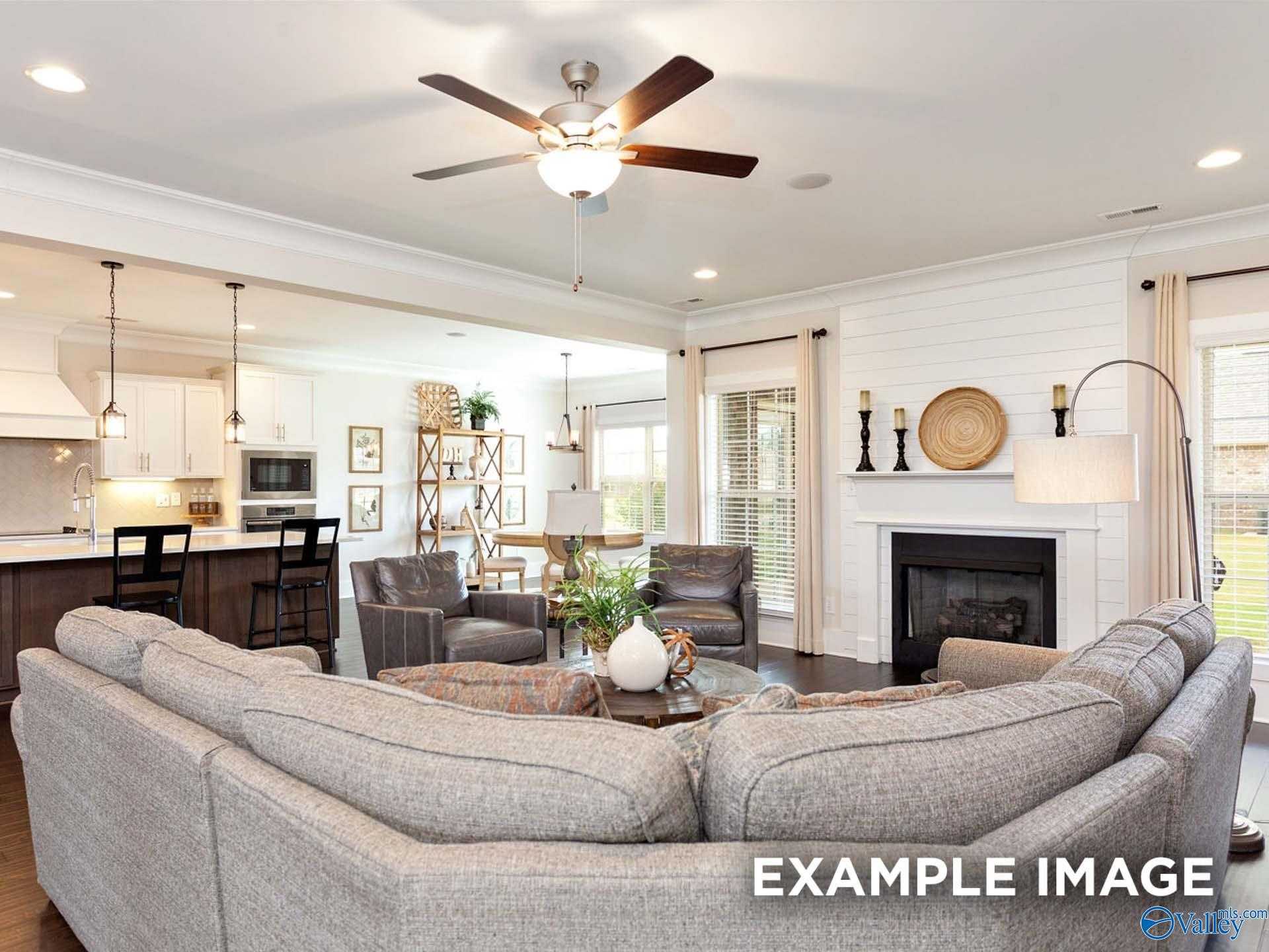 Cozy open-concept living room with gray sectional sofa, fireplace, and kitchen island in The Finleigh 3-bedroom home, Meridianville, Alabama