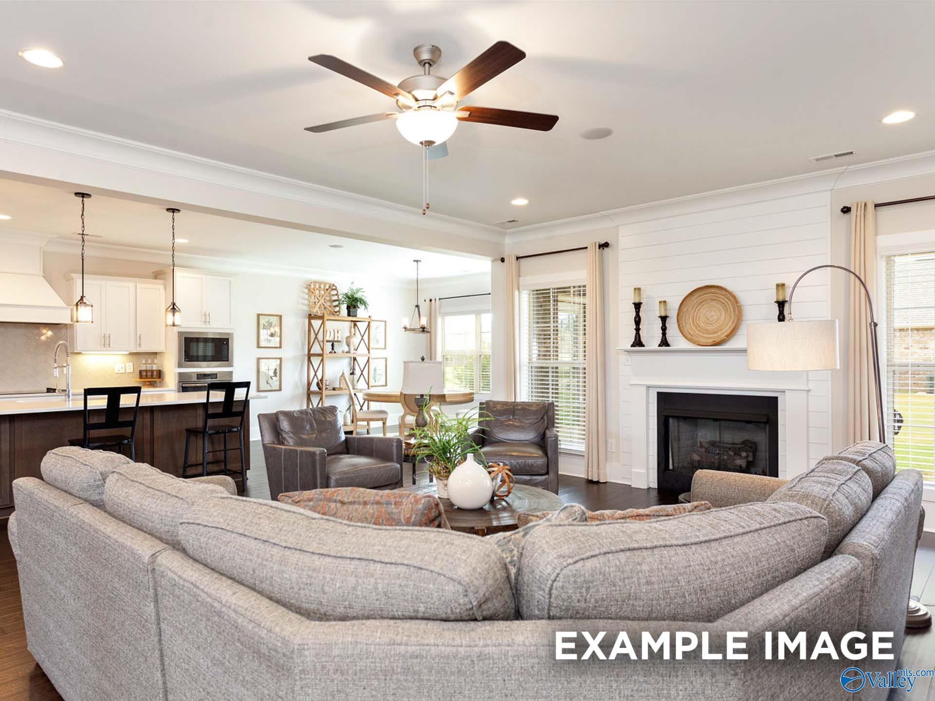 Open-concept living room with gray sectional sofa, fireplace, and adjacent kitchen island in Davidson Homes The Finleigh, Meridianville, Alabama