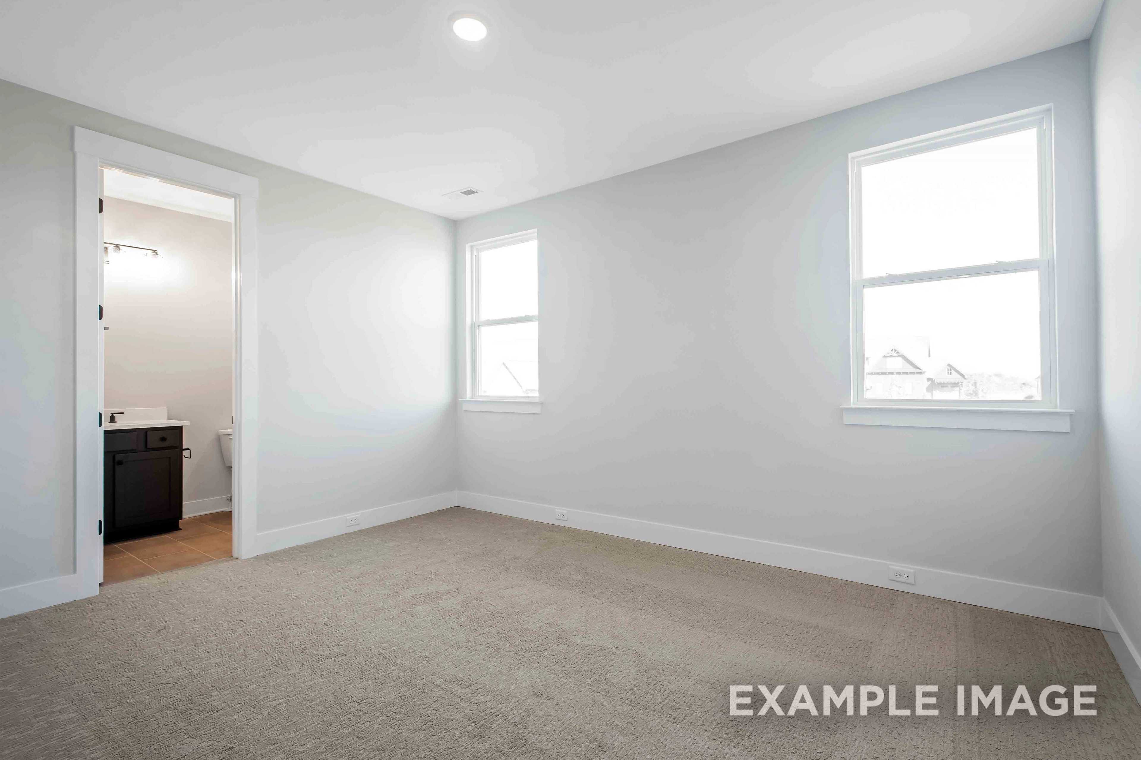Spacious master bedroom in The Alston A featuring en-suite bath, light gray walls, double windows, and plush carpet