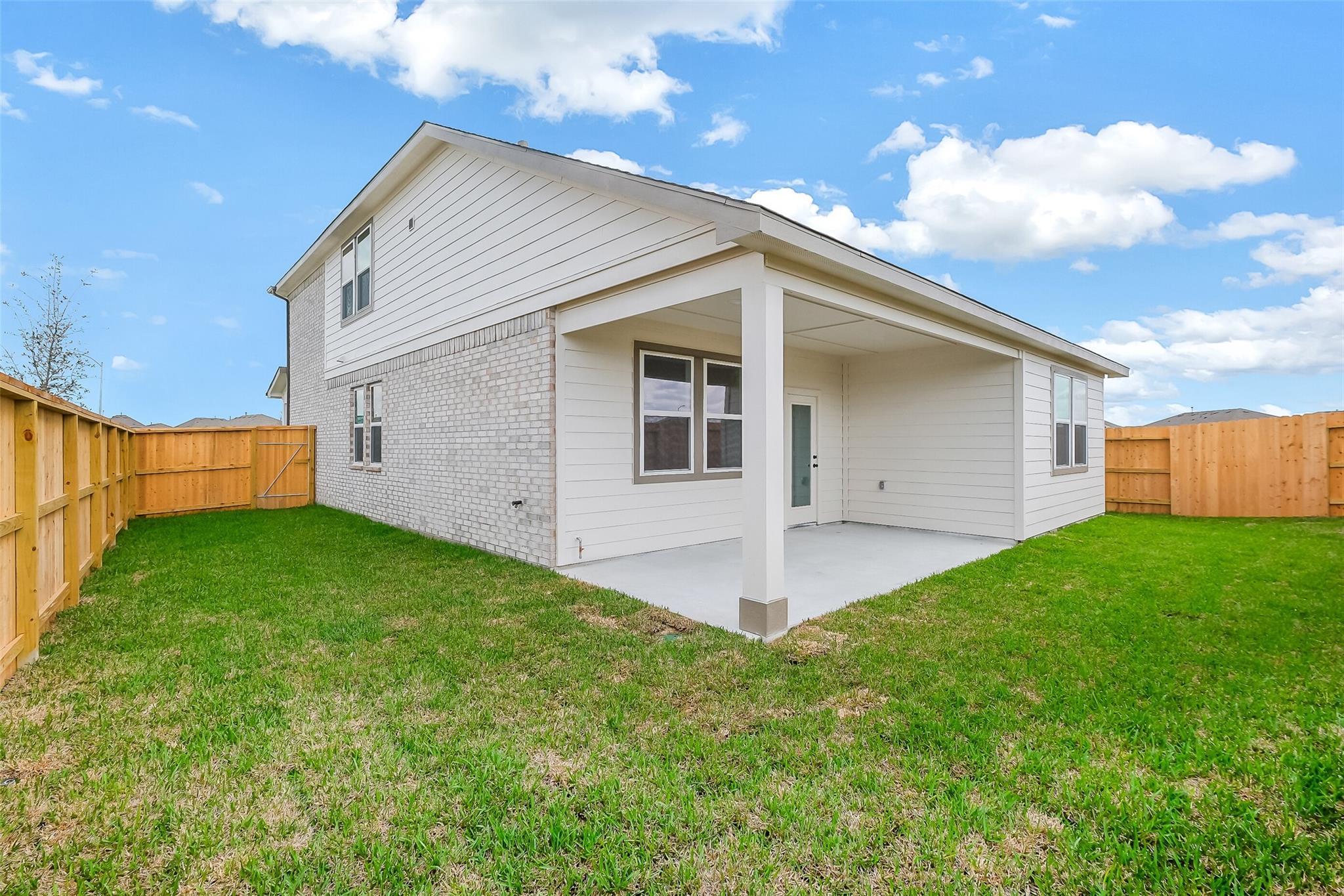 Two-story home back exterior with covered patio, brick accents, and fenced grassy backyard in Emberly, Beasley, Texas Davidson Homes The Tierra B