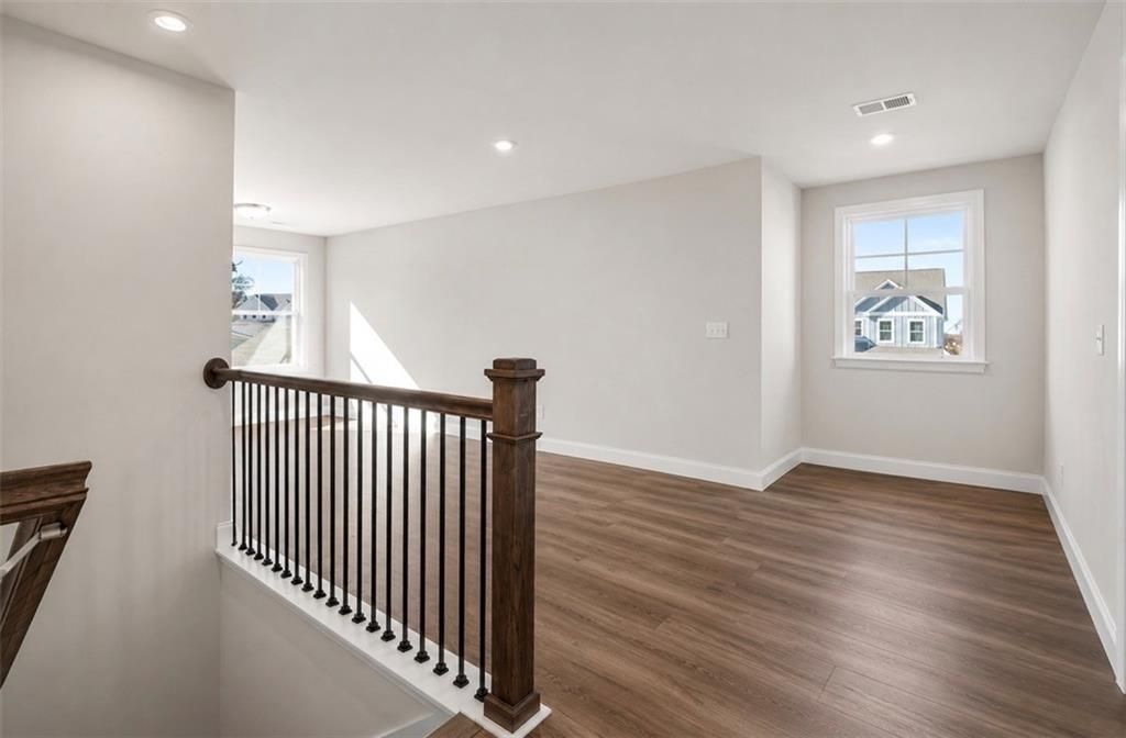 Spacious loft area with wood-style flooring and iron baluster railing in The Ash C floor plan at Wehunt Meadows, Hoschton.