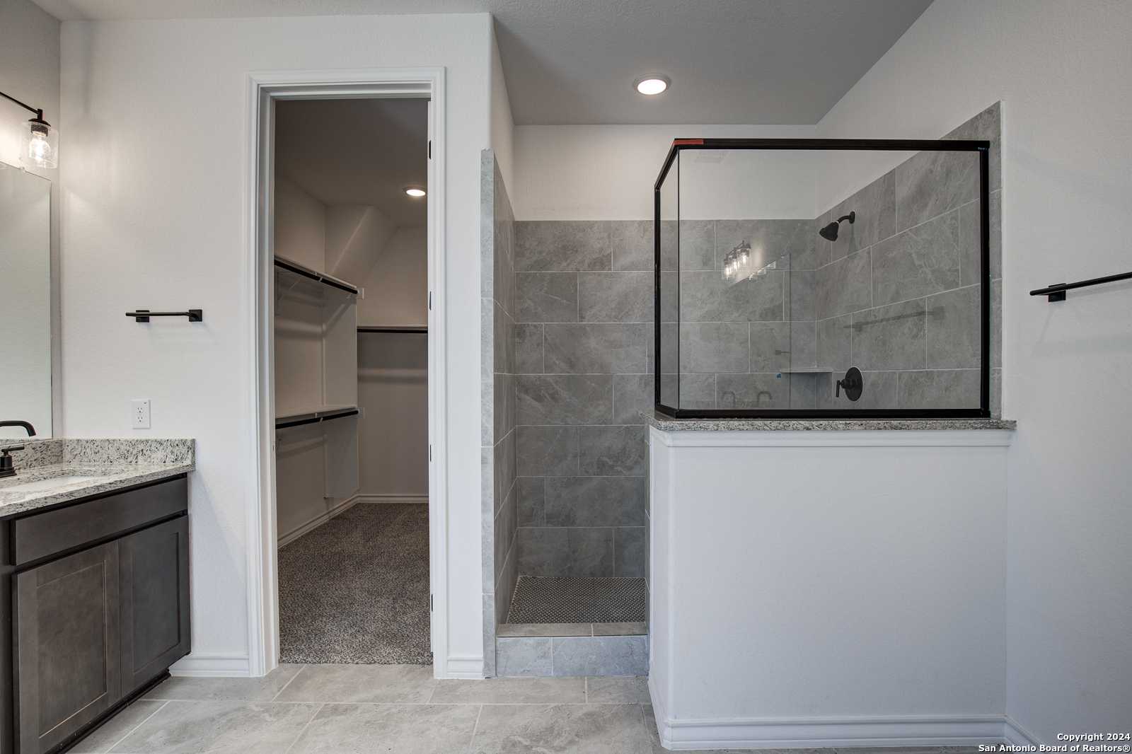 Modern master bathroom with frameless glass shower, gray tile, dual vanity, and walk-in closet in Davidson Homes The Garner B, Castroville, Texas
