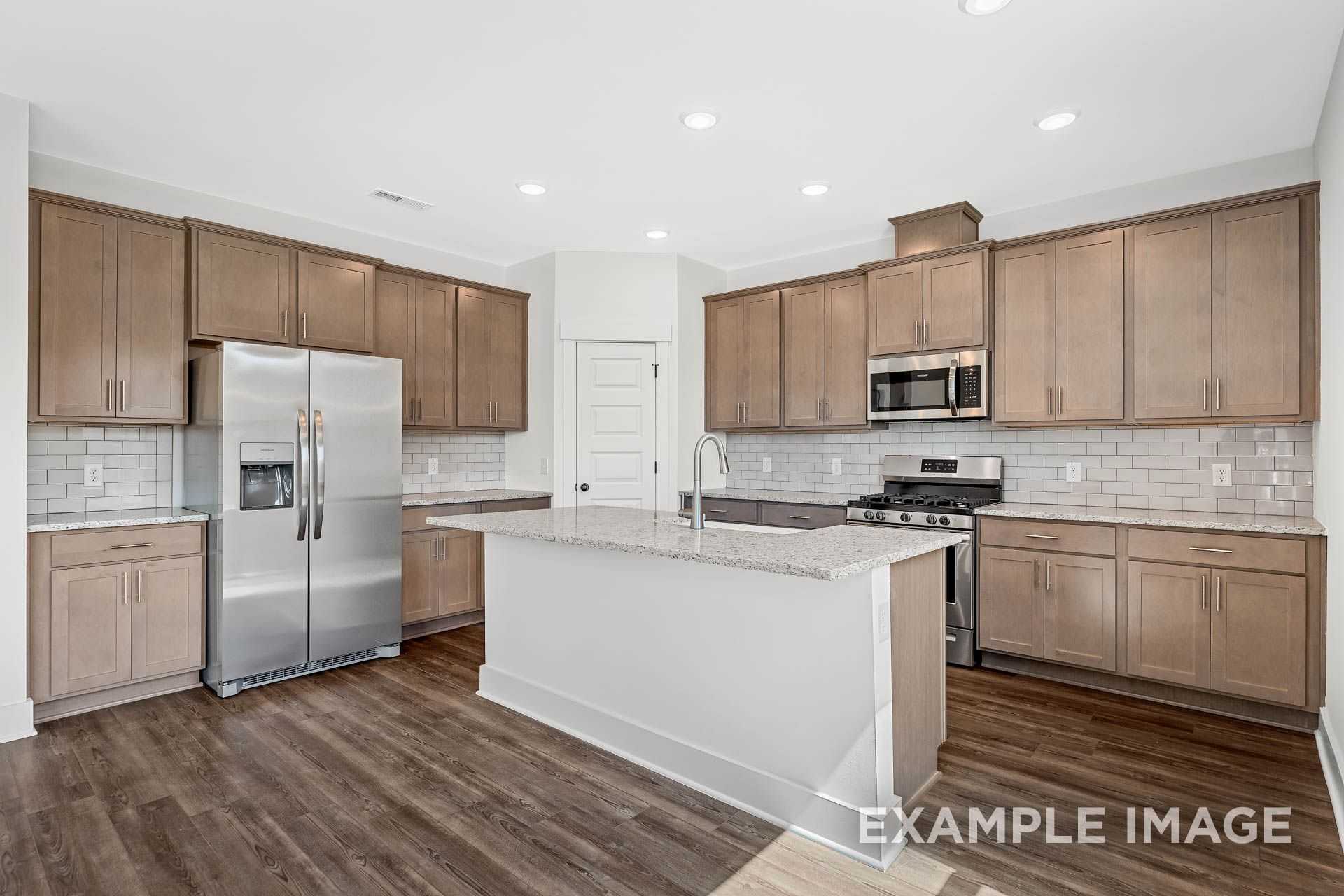 Modern kitchen in The Logan B with light wood cabinets, stainless steel appliances, quartz island, and subway tile backsplash