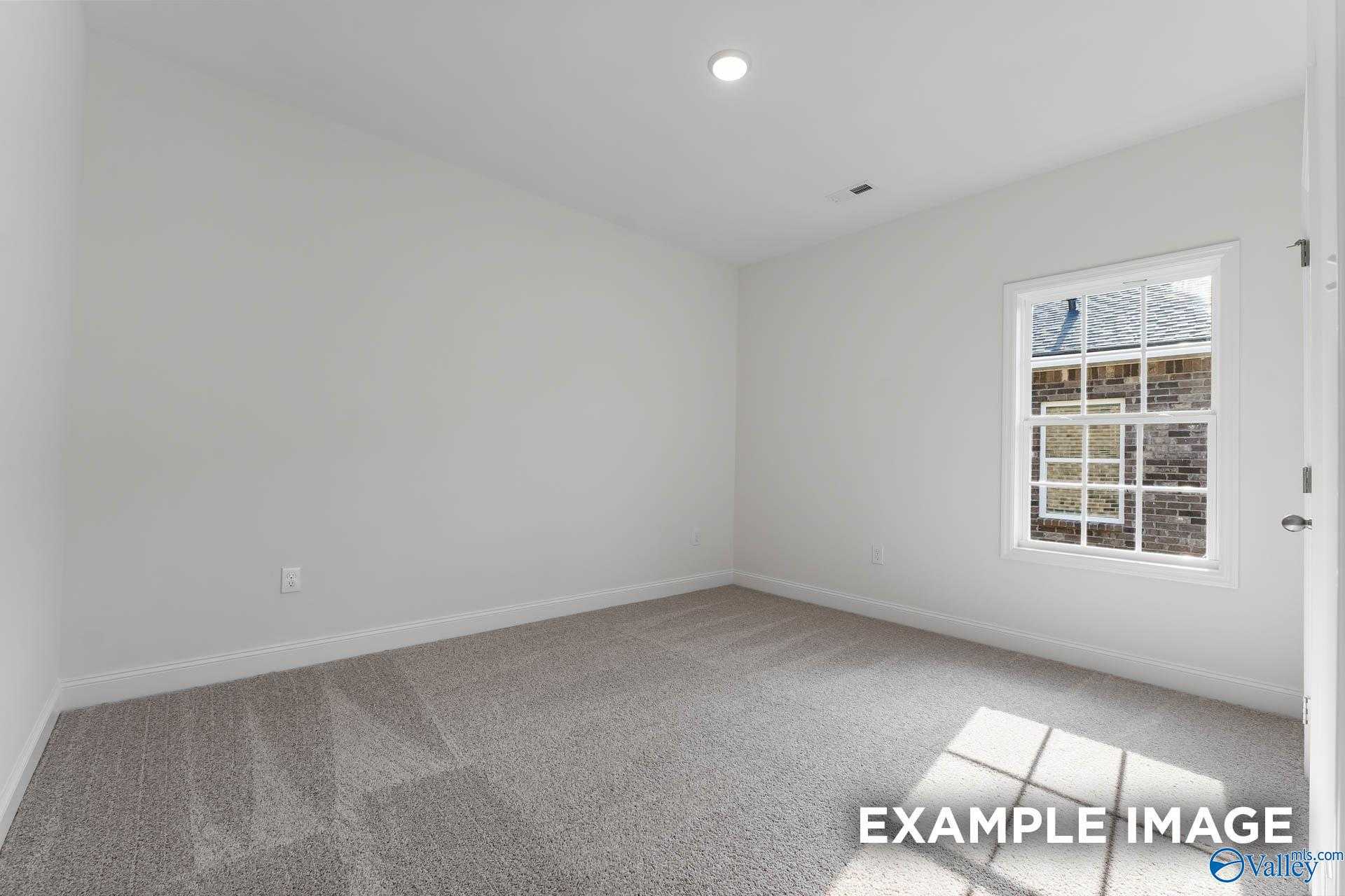 Bright empty bedroom with white walls, beige carpet, large window and natural light in Davidson Homes The Daphne V, Athens, Alabama