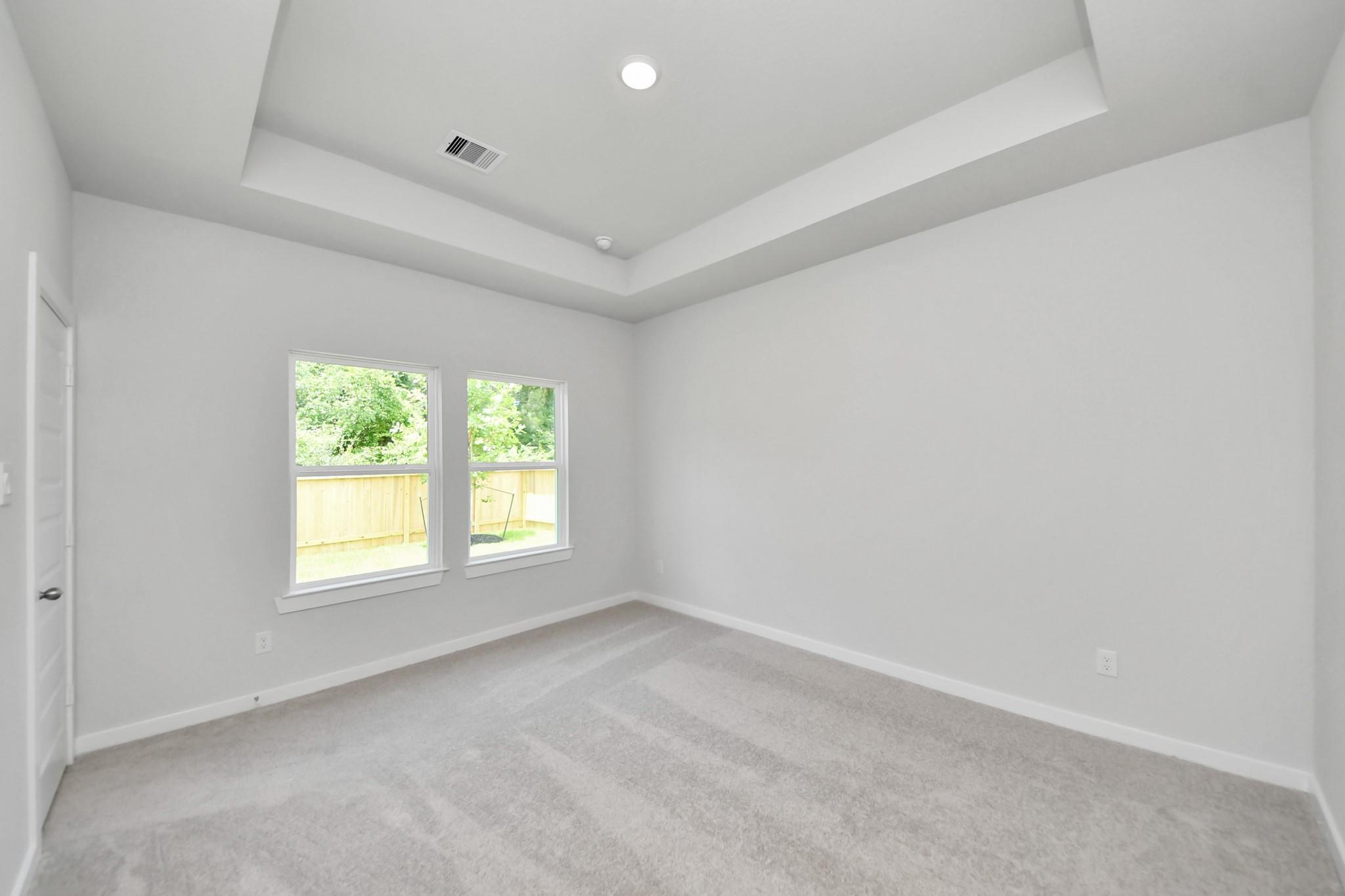 Bright bedroom with tray ceiling and plush carpet in The Blanco E floor plan at Caney Creek Place, Conroe, Texas.