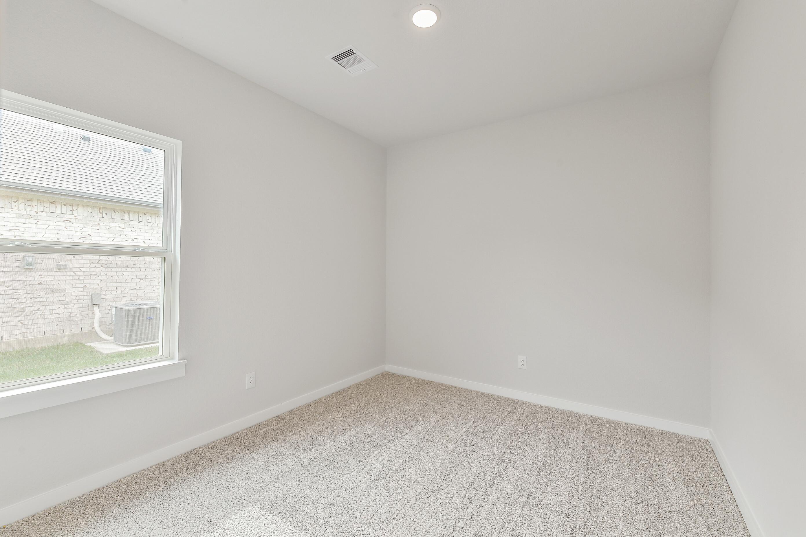 Empty secondary bedroom featuring beige carpet, light walls, and large window in Davidson Homes The Colorado G, Magnolia, Texas