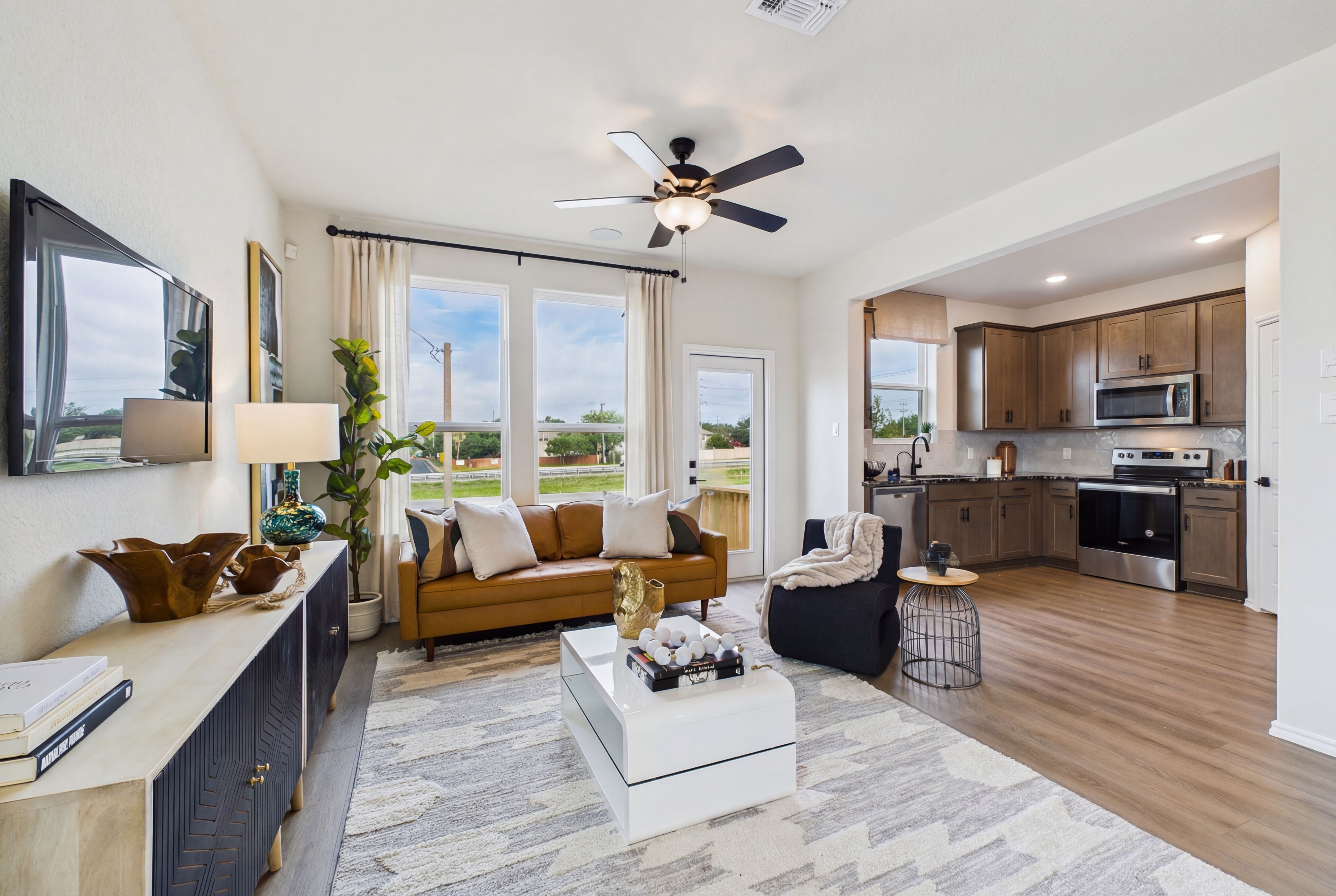 Open-concept living room and kitchen at Meadows at Oak Creek in San Antonio TX with brown leather sofa, hardwood floors, ceiling fans