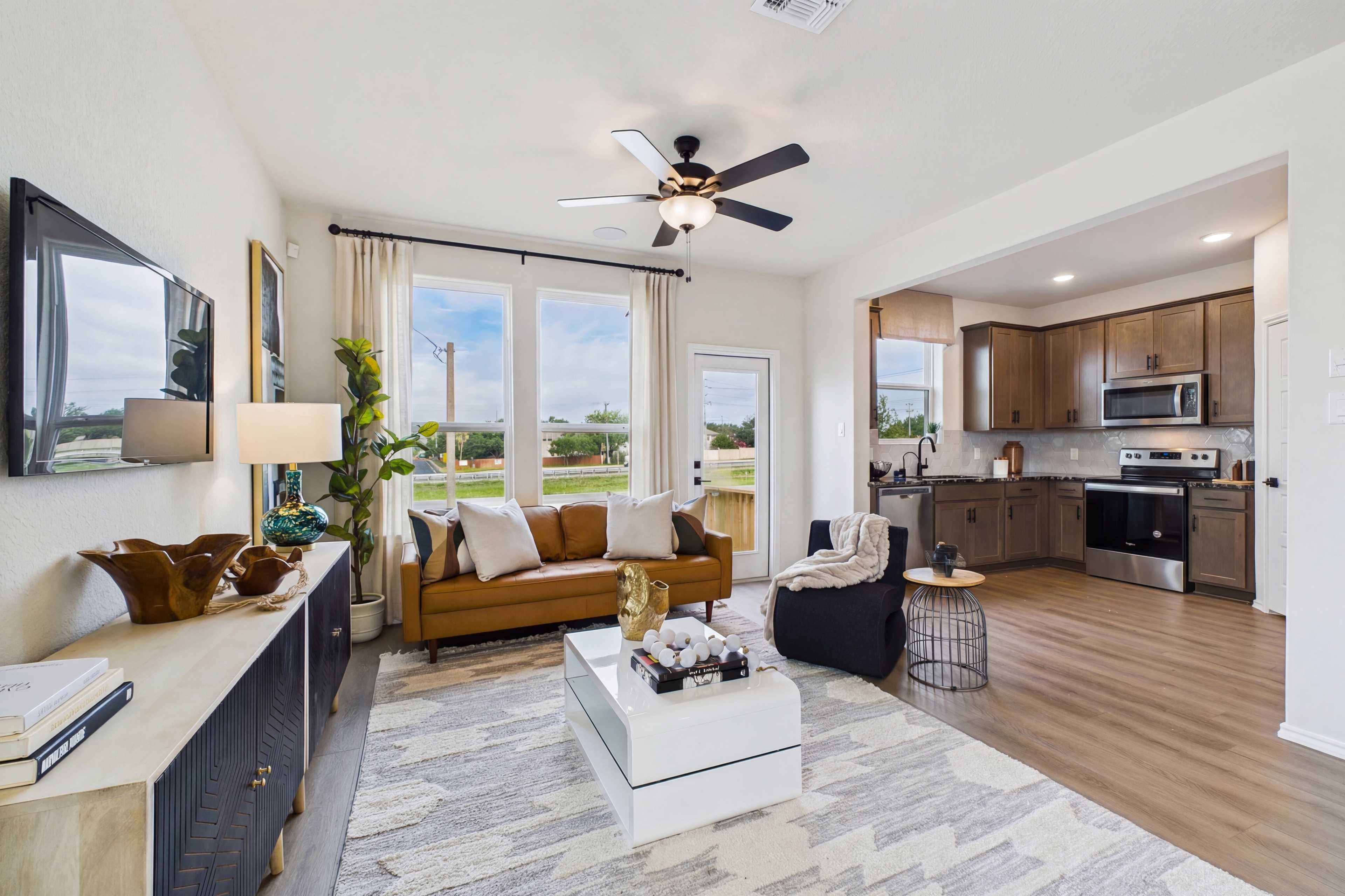 Open-concept living room and kitchen at Meadows at Oak Creek in San Antonio TX with brown leather sofa, hardwood floors, ceiling fans
