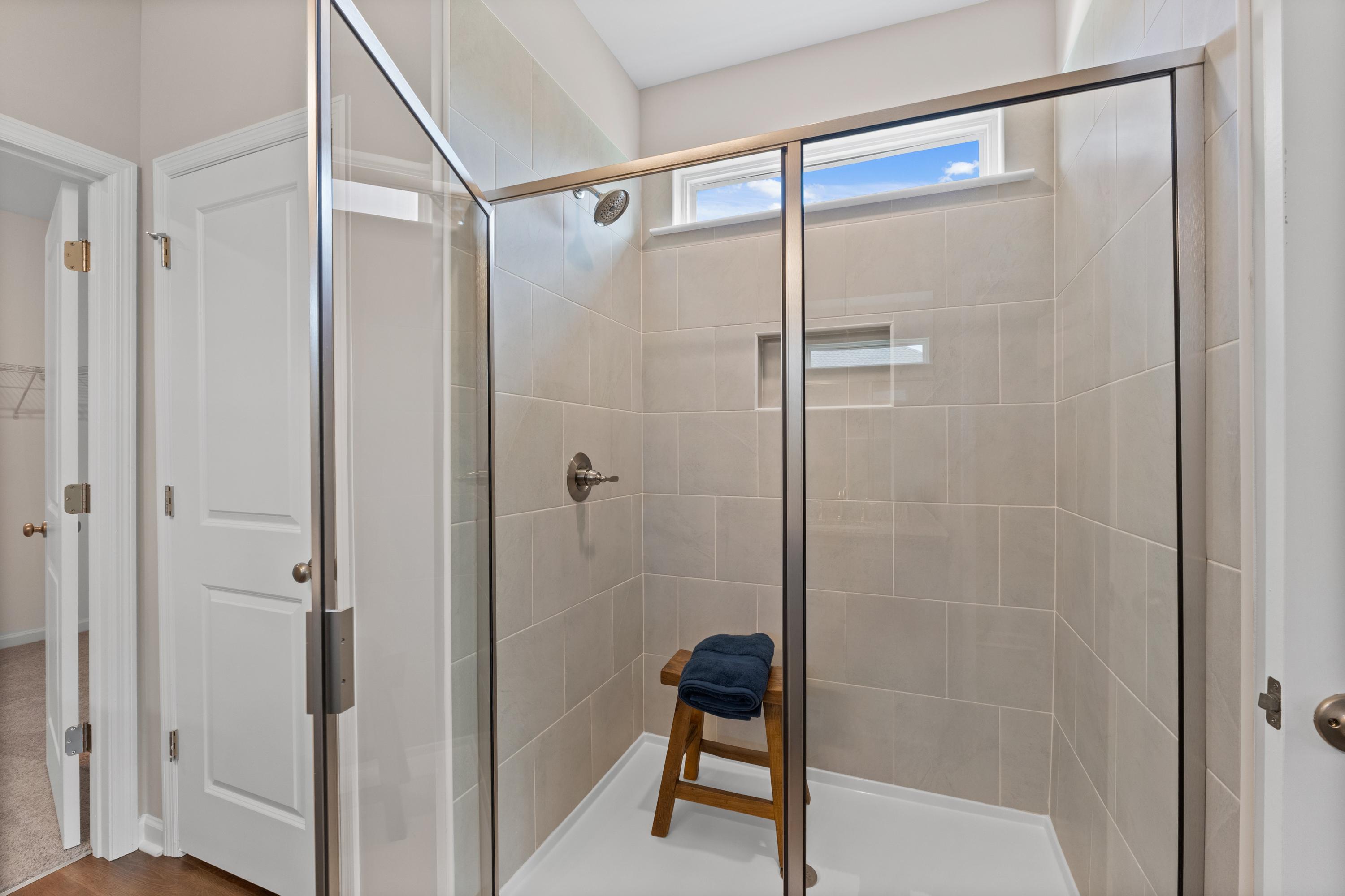 Spacious walk-in shower at Riverton Preserve in Huntsville AL featuring glass enclosure, beige tile walls, wooden bench, and niche shelf
