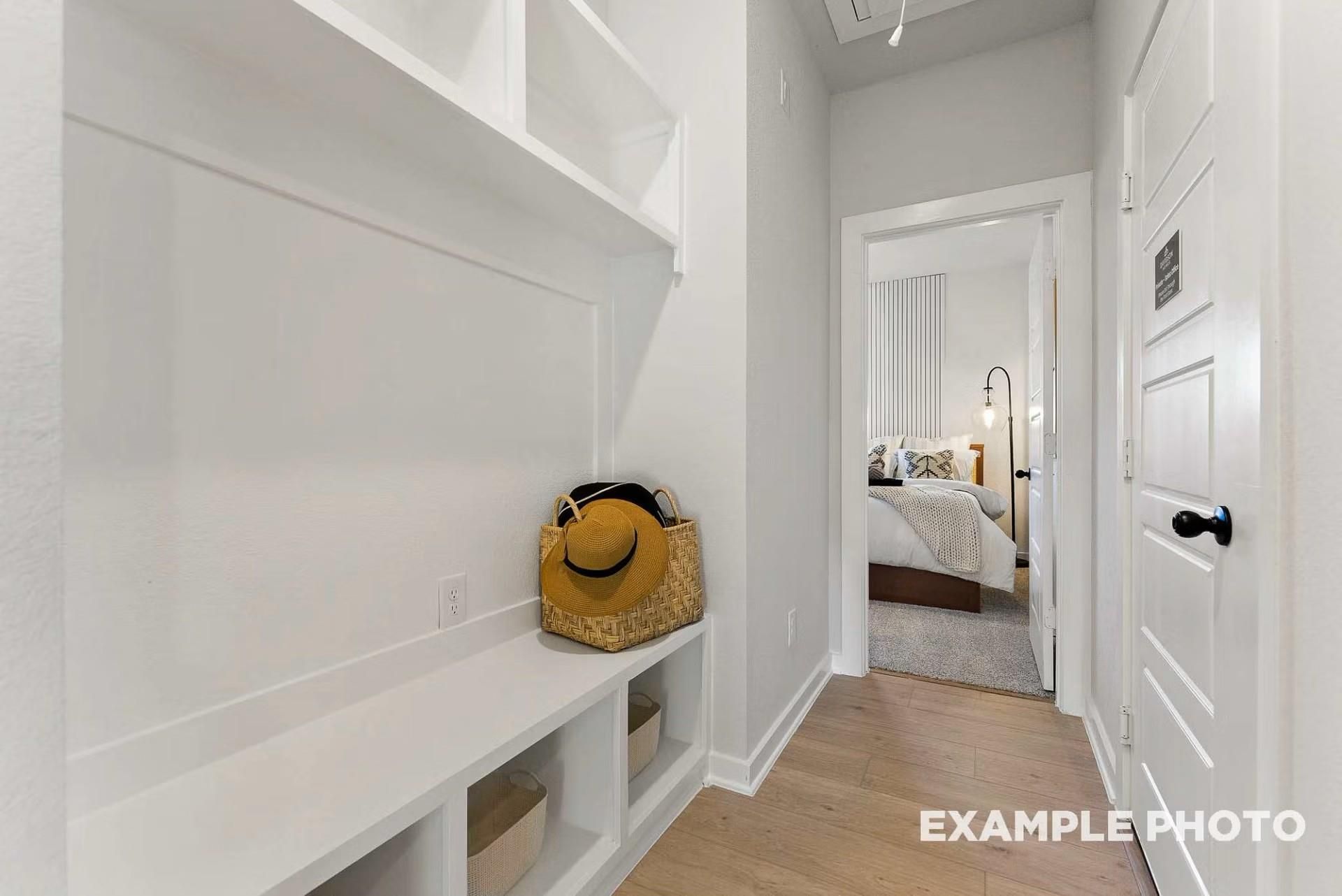 White mudroom with built-in benches, shelves, and storage basket leading to cozy bedroom in Davidson Homes Everett C, Dayton, Texas