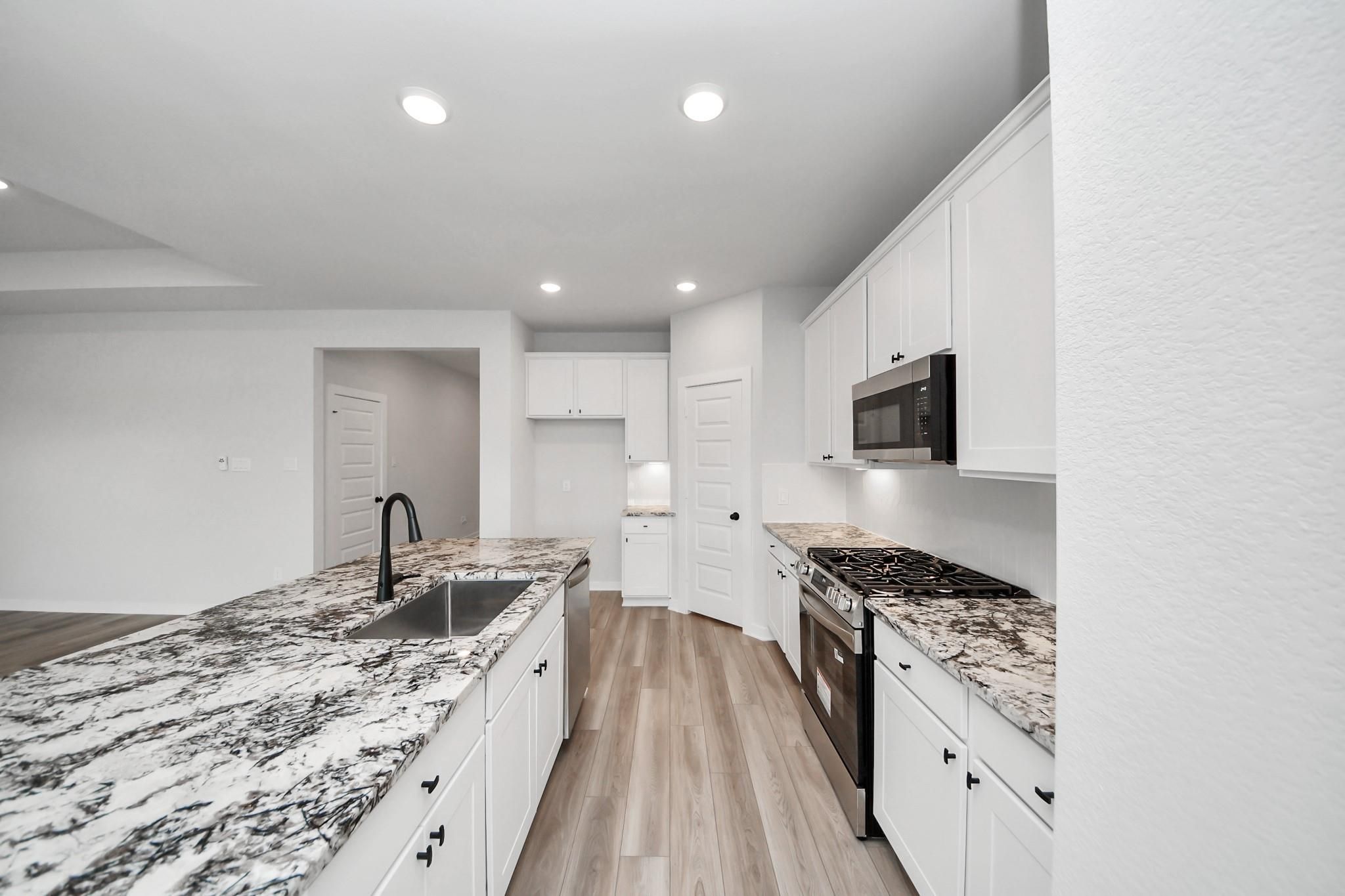 Modern kitchen with white cabinets, granite countertops, and stainless appliances in The Everett C home, River Ranch Meadows.