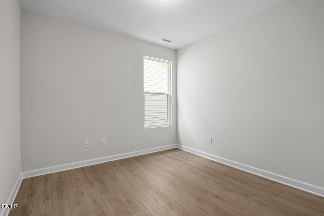 Bright empty bedroom with wood-look flooring and window in Davidson Homes The Daphne D, Woodland Crossing, Zebulon NC