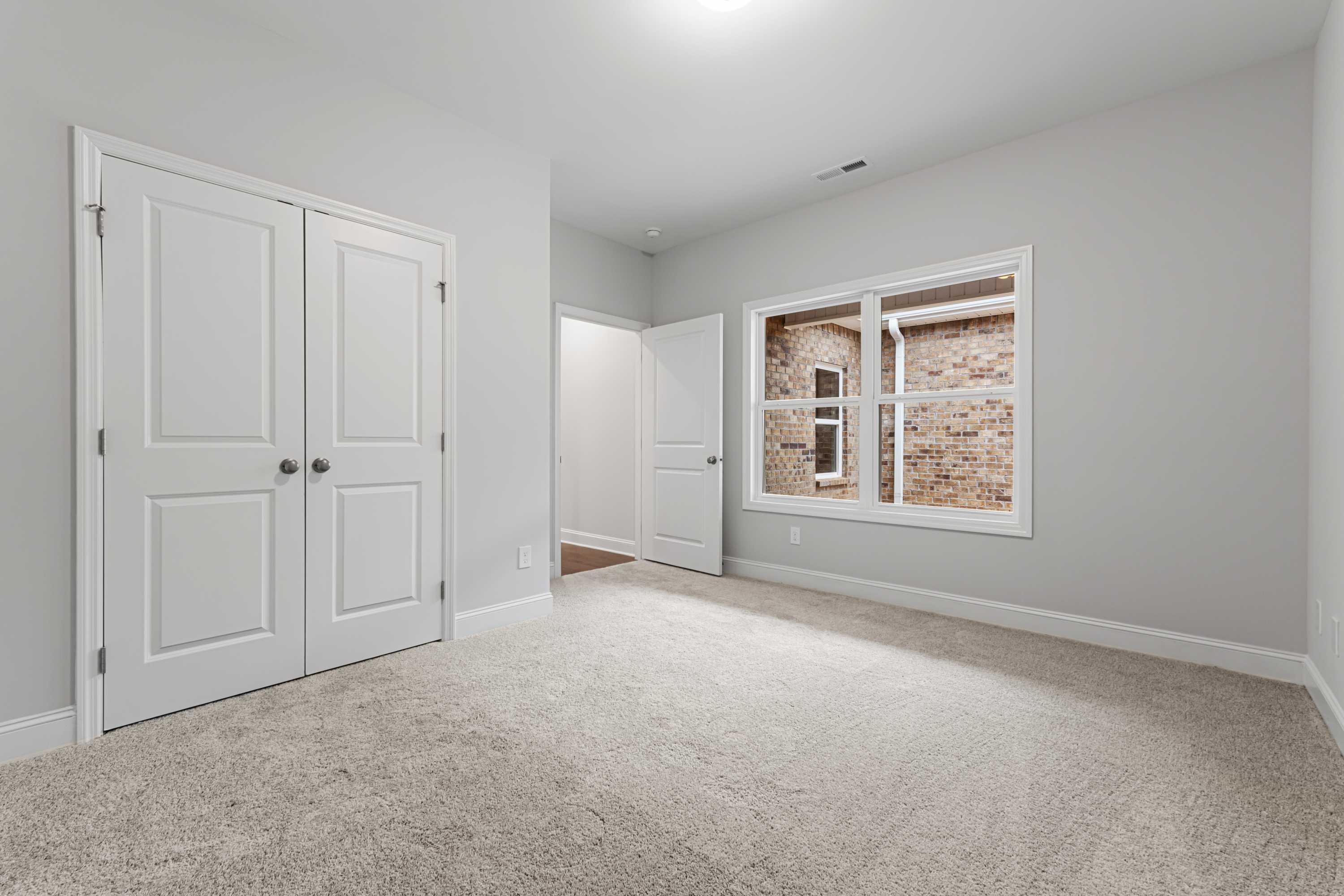 Spacious master bedroom in The Copeland B with light gray walls, white double closet doors, and brick-accented window