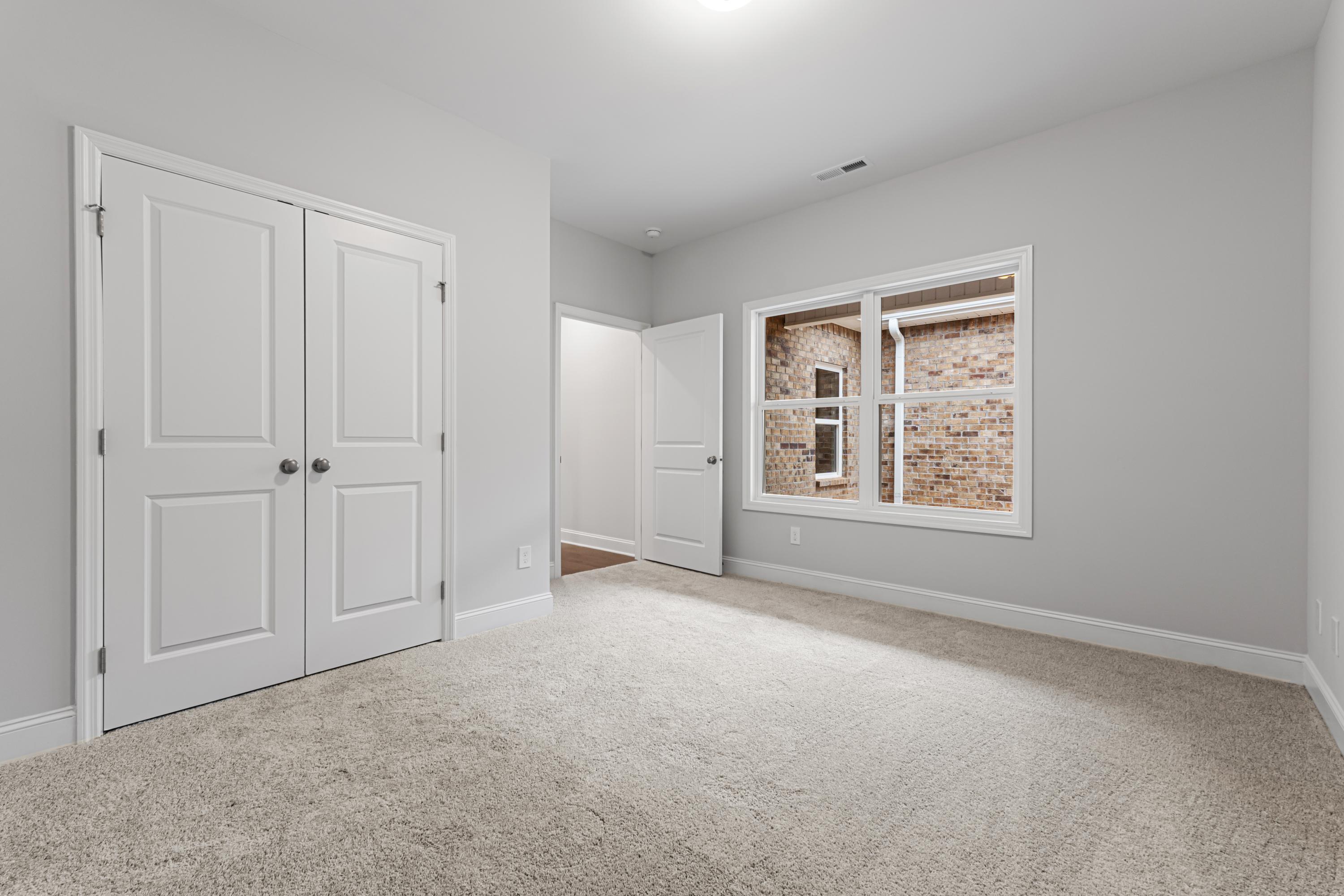 Spacious master bedroom in The Copeland C with light gray walls, white double closet doors, and brick-accented window