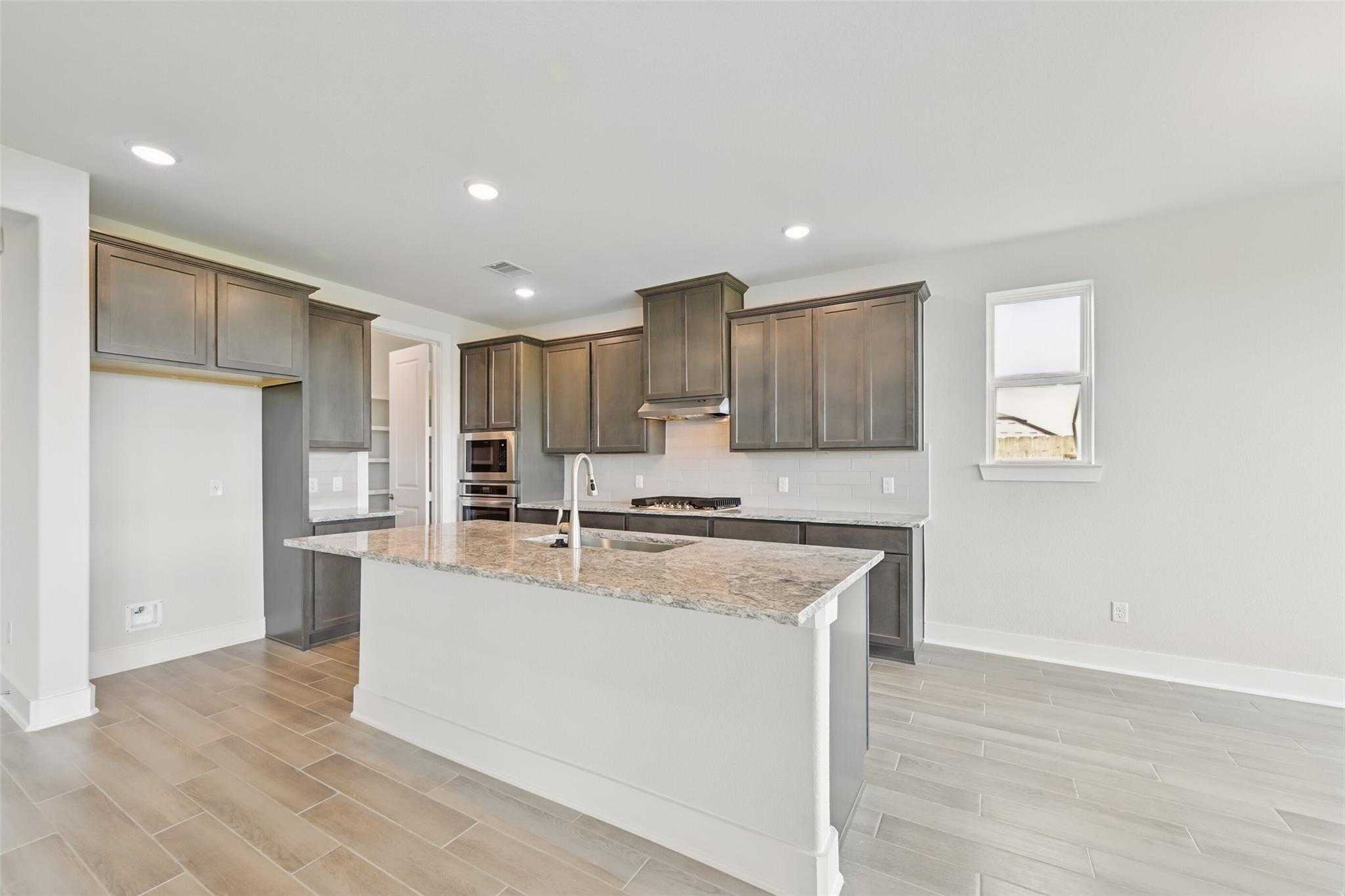 Modern kitchen with gray shaker cabinets, granite island sink, stainless appliances in Davidson Homes Philip A, Lago Mar, Texas City