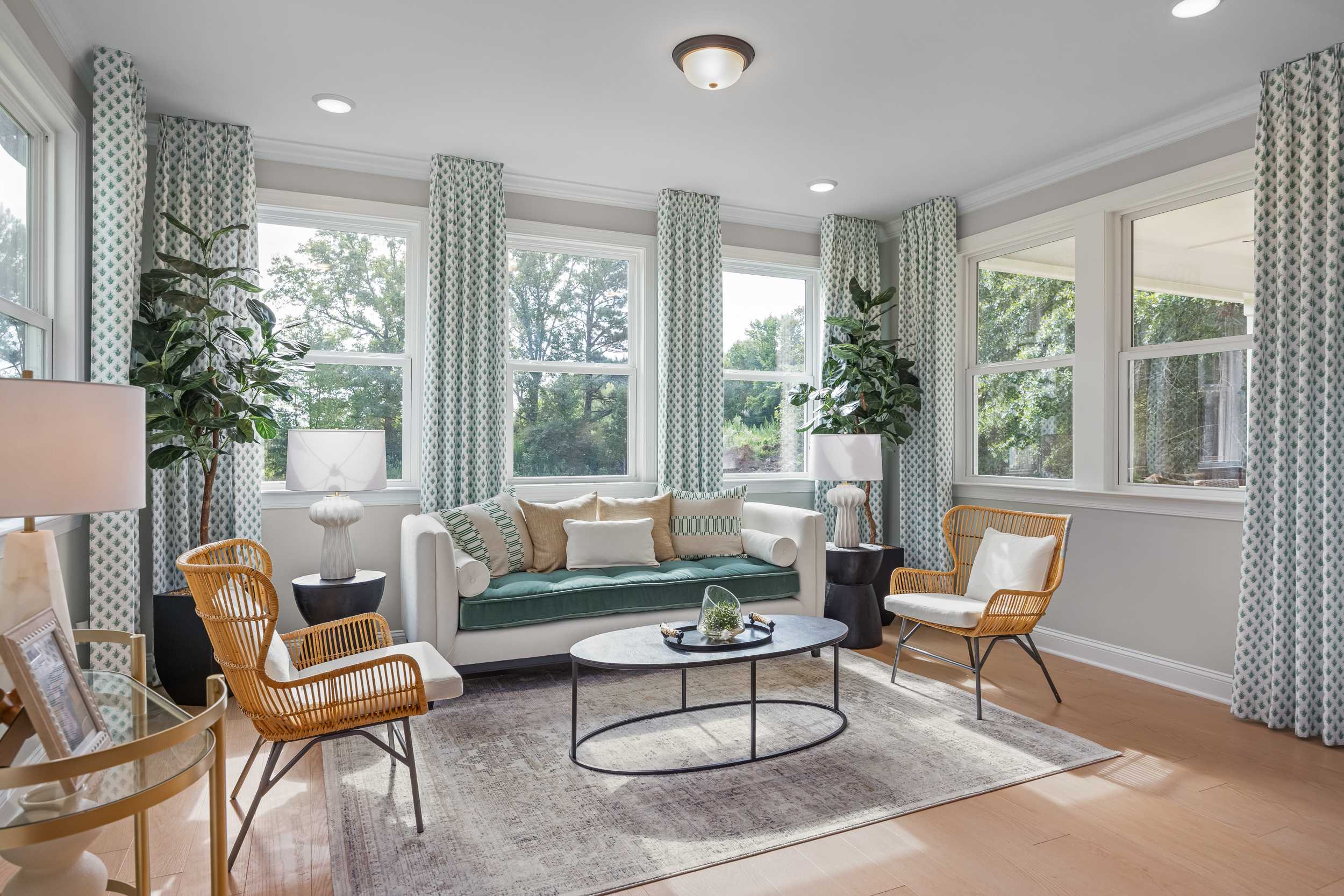 Sunlit sunroom at Laneridge Estates in Raleigh NC with large windows, blue curtains, beige sofa, wicker chairs and potted plants
