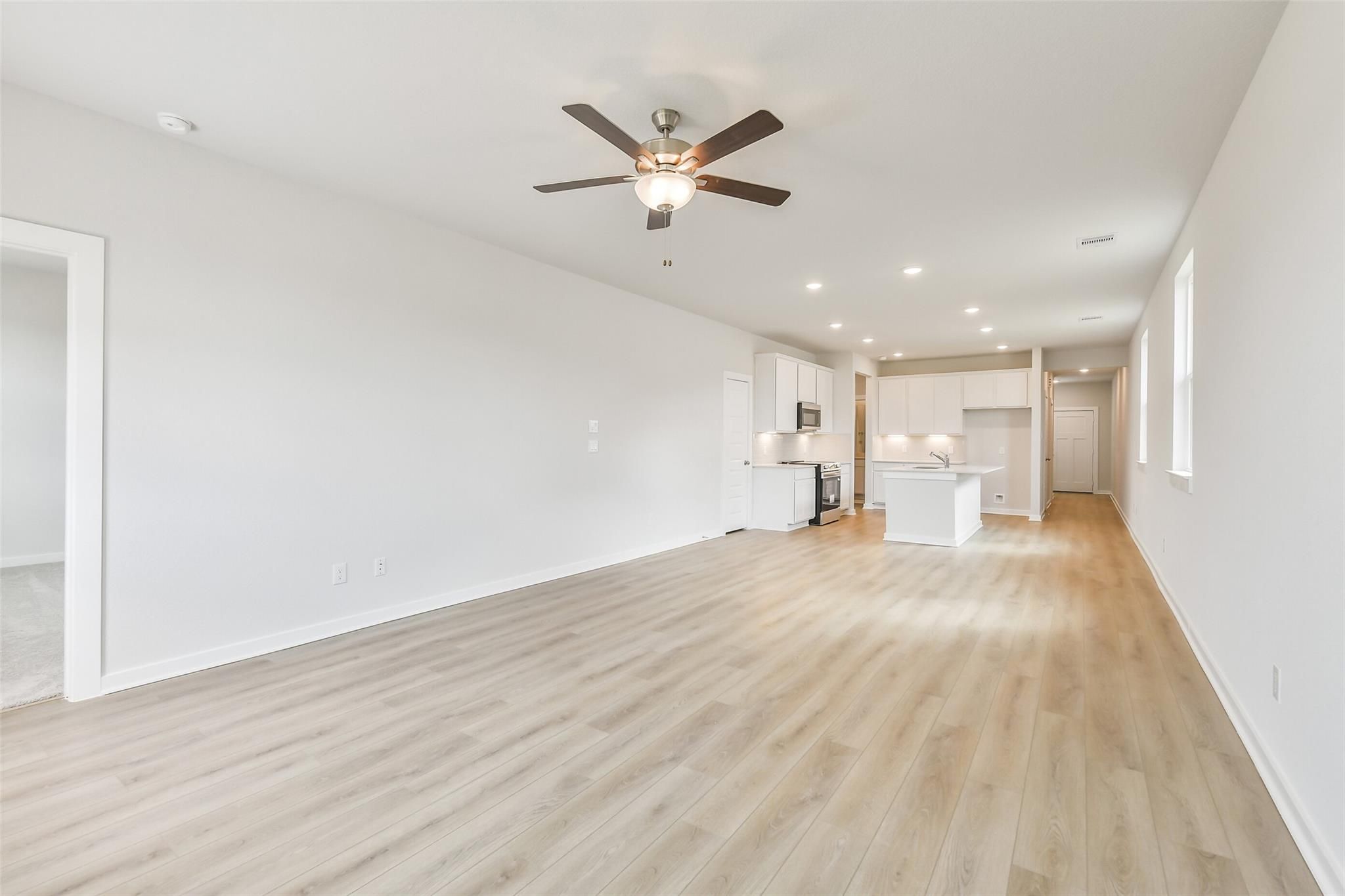 Spacious open living and kitchen area with white cabinets, ceiling fan, and hardwood floors in Davidson Homes The Frio G, Cleveland, TX