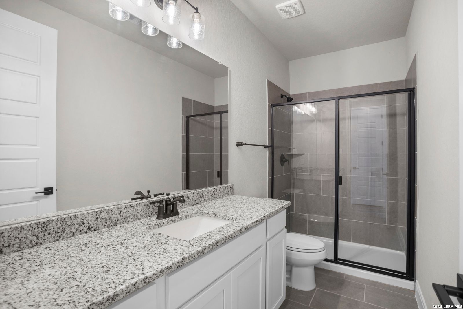 Modern bathroom with granite vanity, white cabinets, and walk-in tiled shower in The Jennings G plan at Ladera, San Antonio.