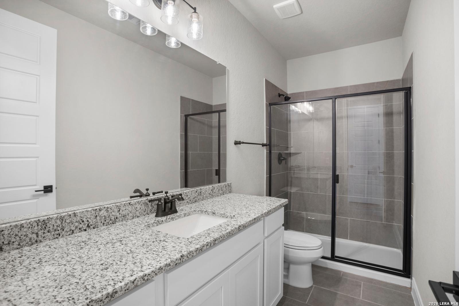 Modern bathroom with granite vanity, white cabinets, and walk-in tiled shower in The Jennings G plan at Ladera, San Antonio.