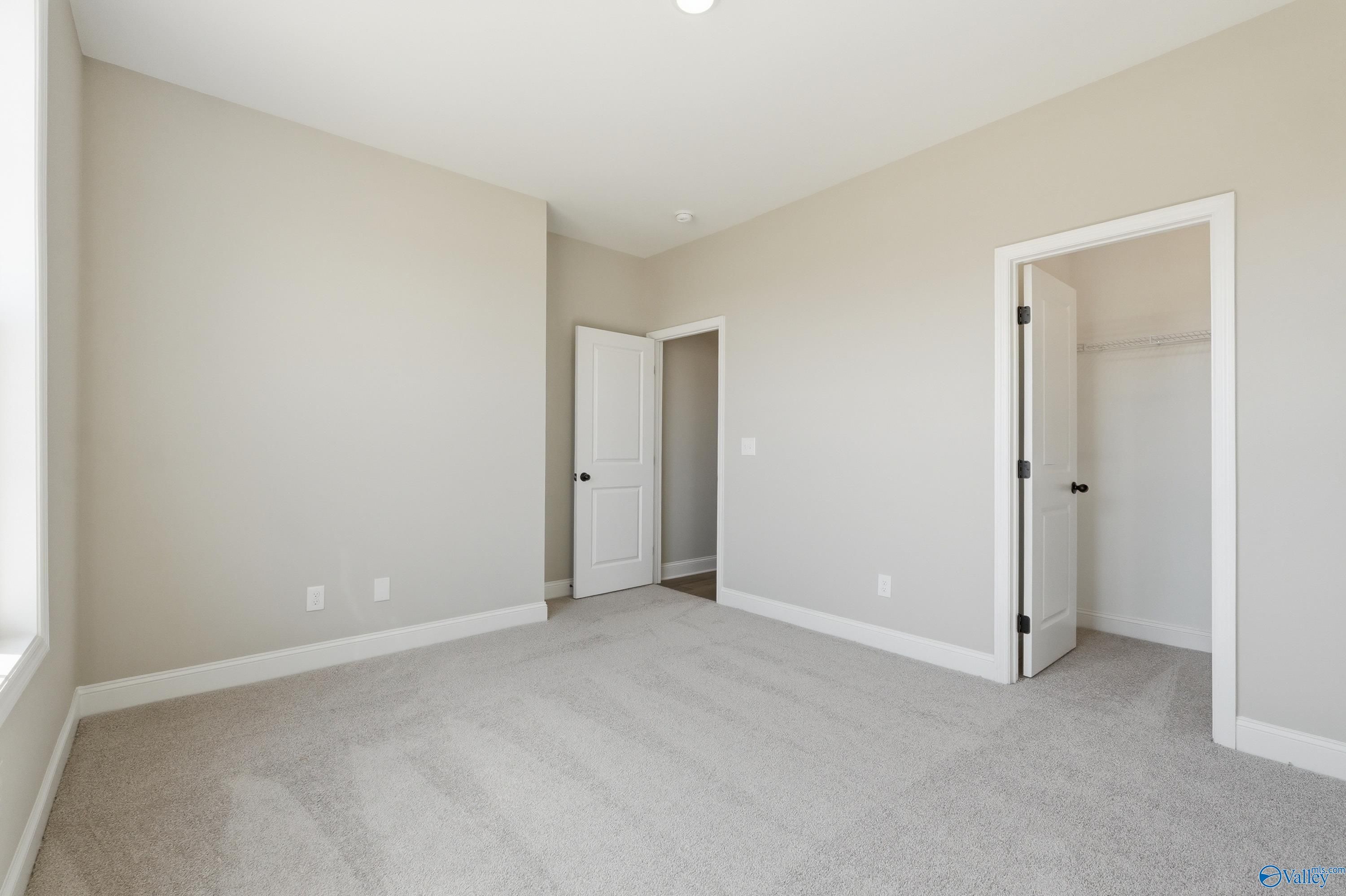 Spacious bedroom with walk-in closet, beige walls, and carpeted floors in Davidson Homes The Rockford, Creekside, Harvest, Alabama