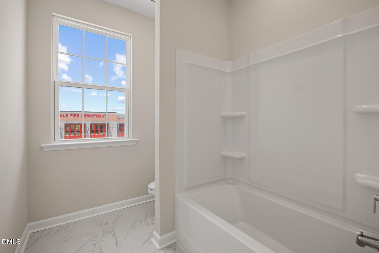 Full bathroom with white tub shower combo and marble-style flooring in The Alexander C floor plan at Forestville Yard.