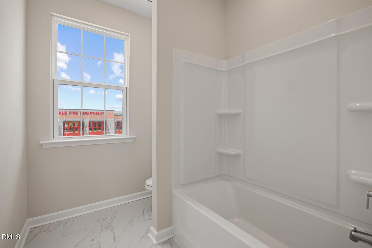Full bathroom with white tub shower combo and marble-style flooring in The Alexander C floor plan at Forestville Yard.