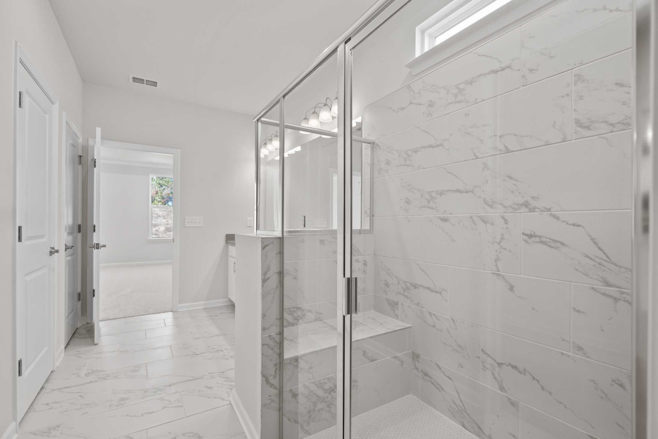 Modern master bathroom in The Dawson C with white marble tiles, frameless glass shower, double vanity, and freestanding tub