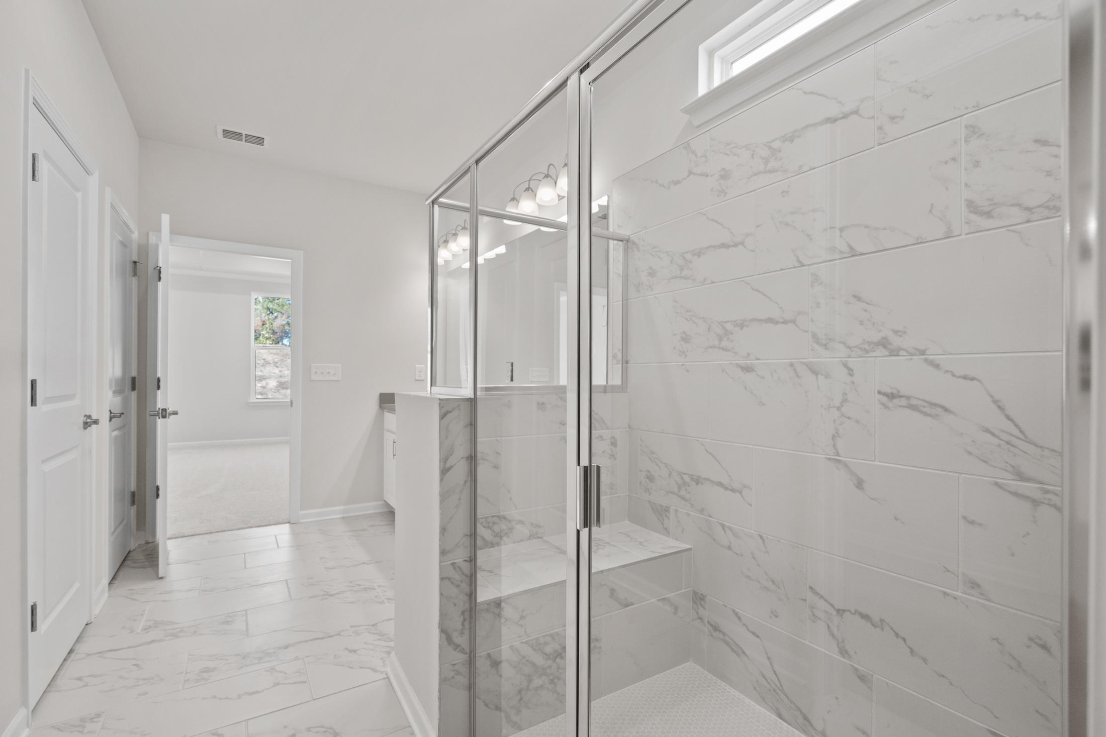 Modern master bathroom in The Dawson C with white marble tiles, frameless glass shower, double vanity, and freestanding tub