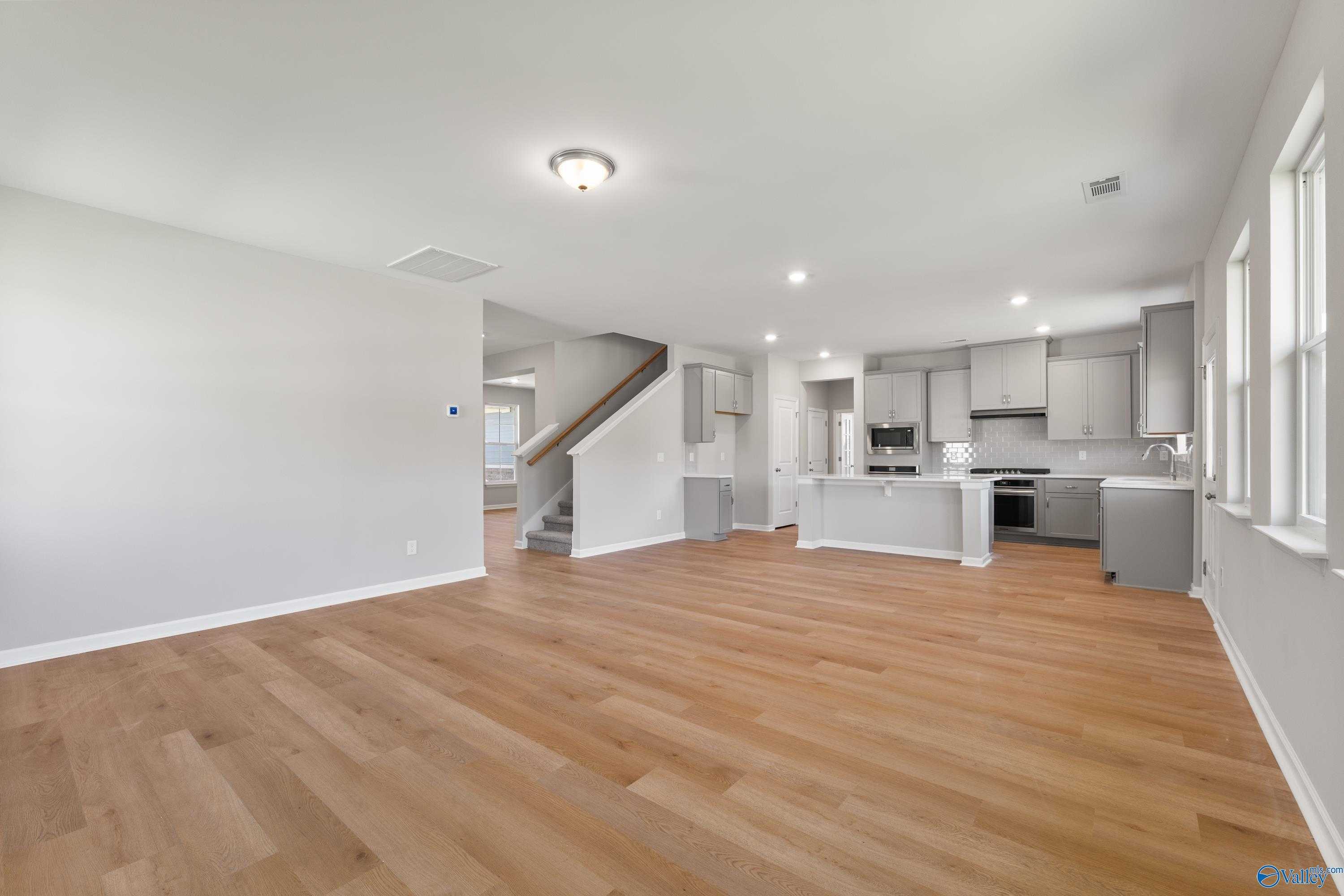 Open-concept kitchen with white shaker cabinets, island, stainless appliances, and hardwood floors in Davidson Homes The Charm, Huntsville AL