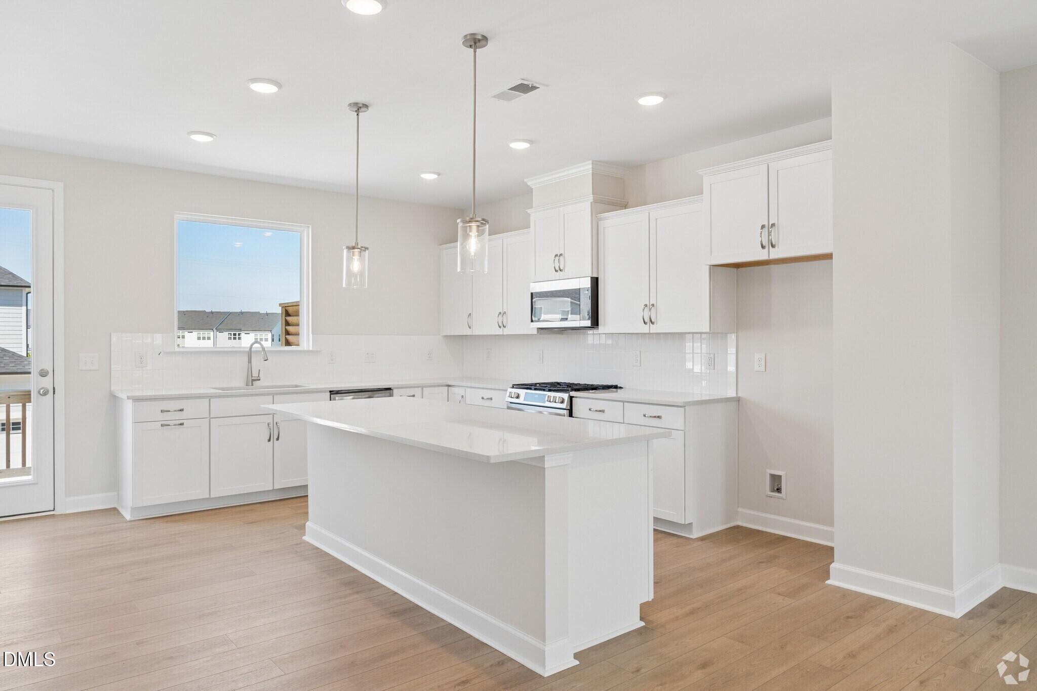 Bright white kitchen with island, pendant lights, and gas range in Davidson Homes The Avery townhome, Knightdale, NC