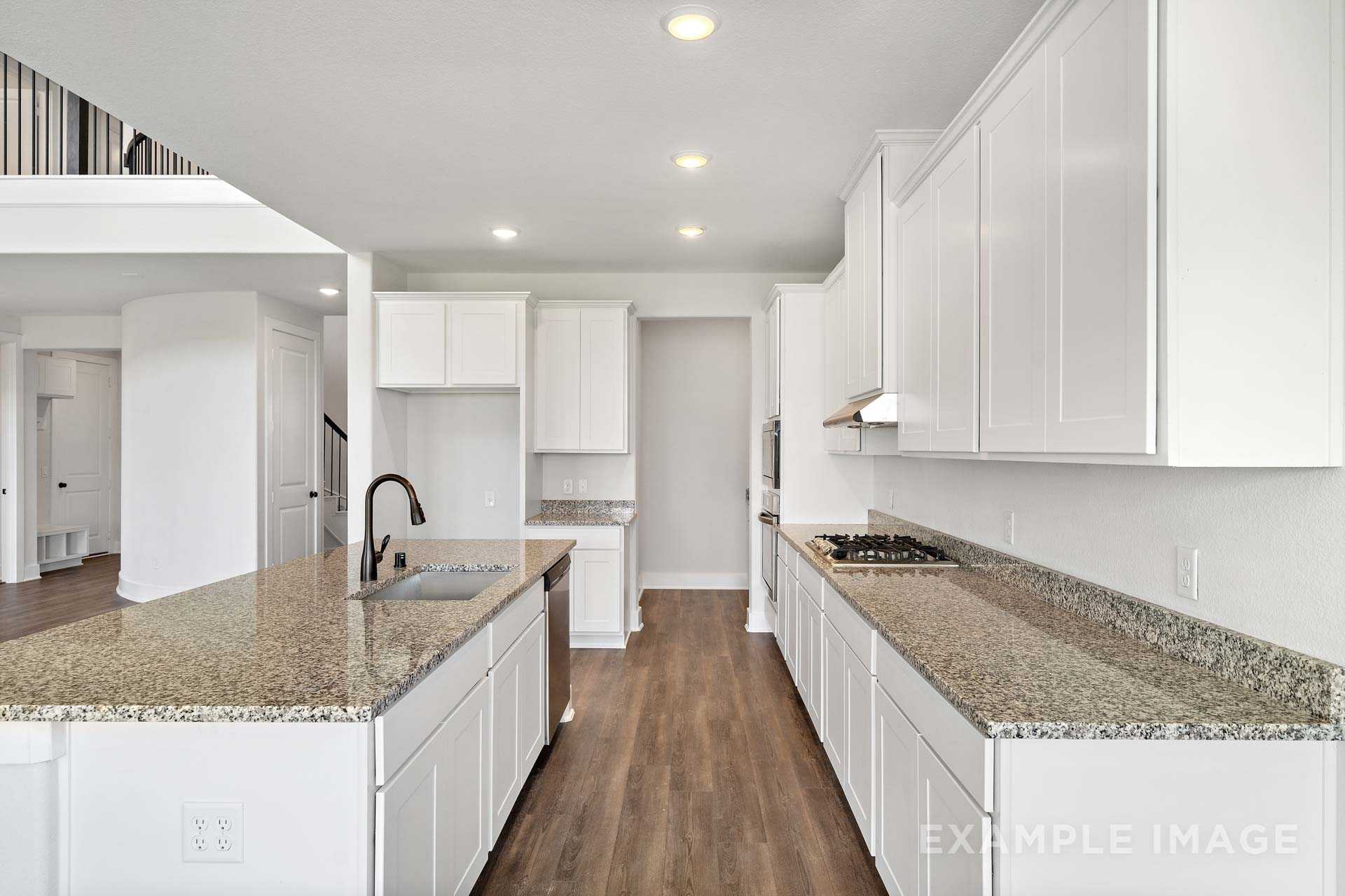 Open-concept kitchen in The Victoria A with white cabinets, granite island sink, gas range, hardwood floors, and loft overlook