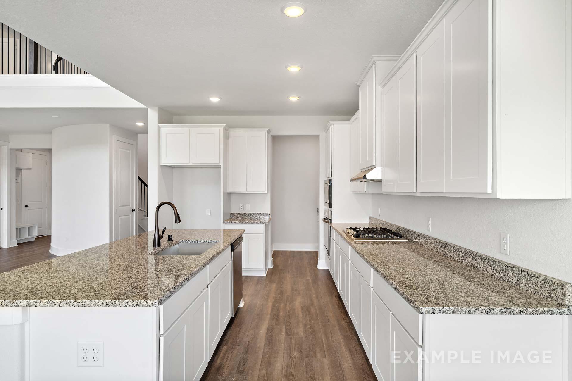 Open-concept kitchen in The Victoria A with white cabinets, granite island sink, gas range, hardwood floors, and loft overlook