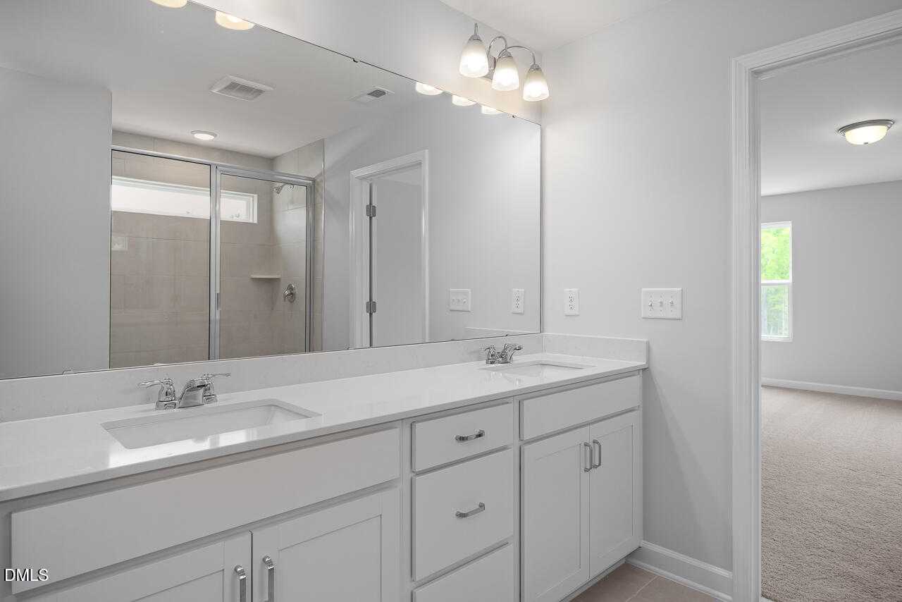 Modern master bathroom with double white vanity, quartz counters, large mirror, and glass shower in The Hickory II B, Zebulon, NC
