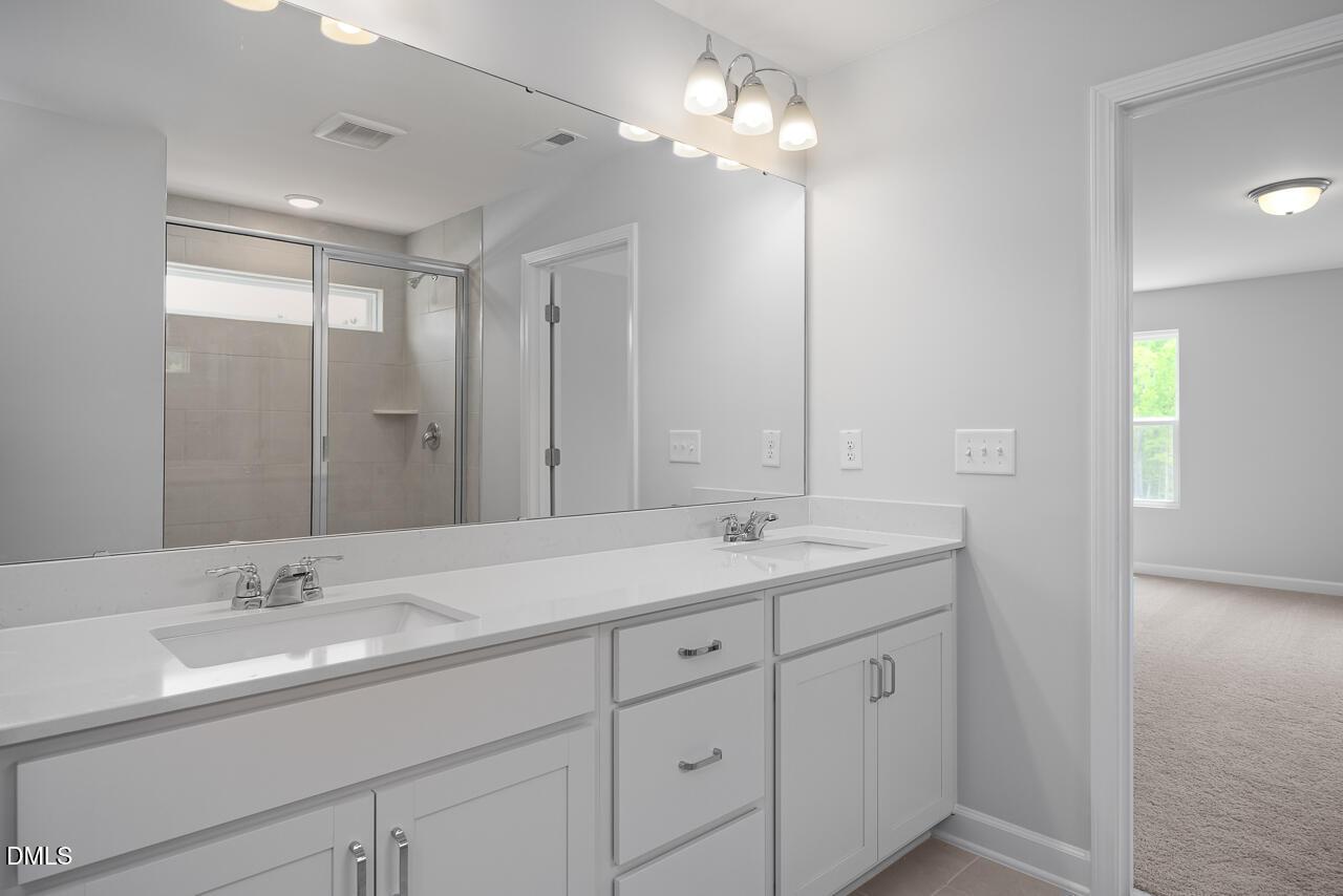 Modern master bathroom featuring double white vanity, quartz counters, large mirror, and frameless glass shower in The Hickory II B, Zebulon, NC
