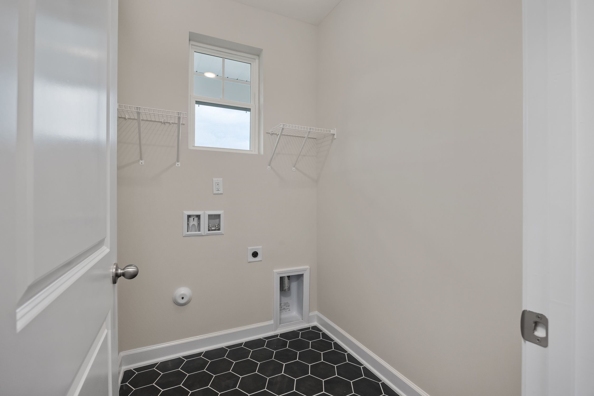 Laundry room with black hexagonal floor tiles and wall shelving at Gregory Village in Lillington, NC by Davidson Homes.