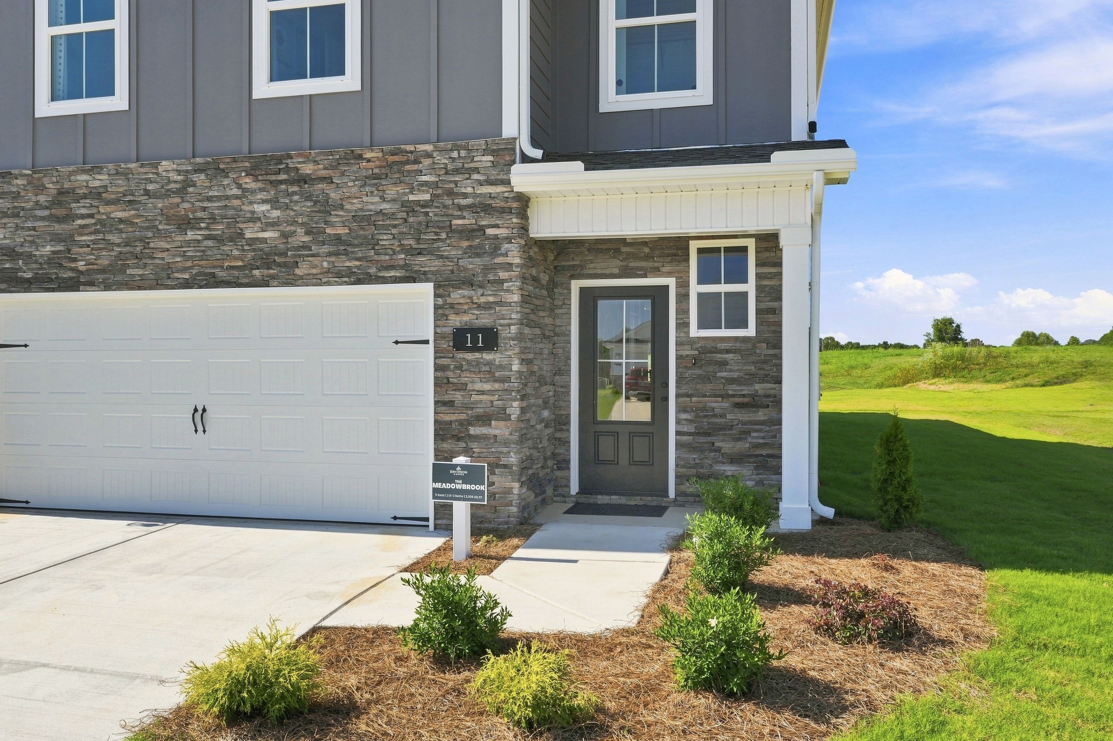 Two-story gray and stone new home exterior at Bailey Park in Fayetteville, TN by Davidson Homes with covered front porch and two-car garage