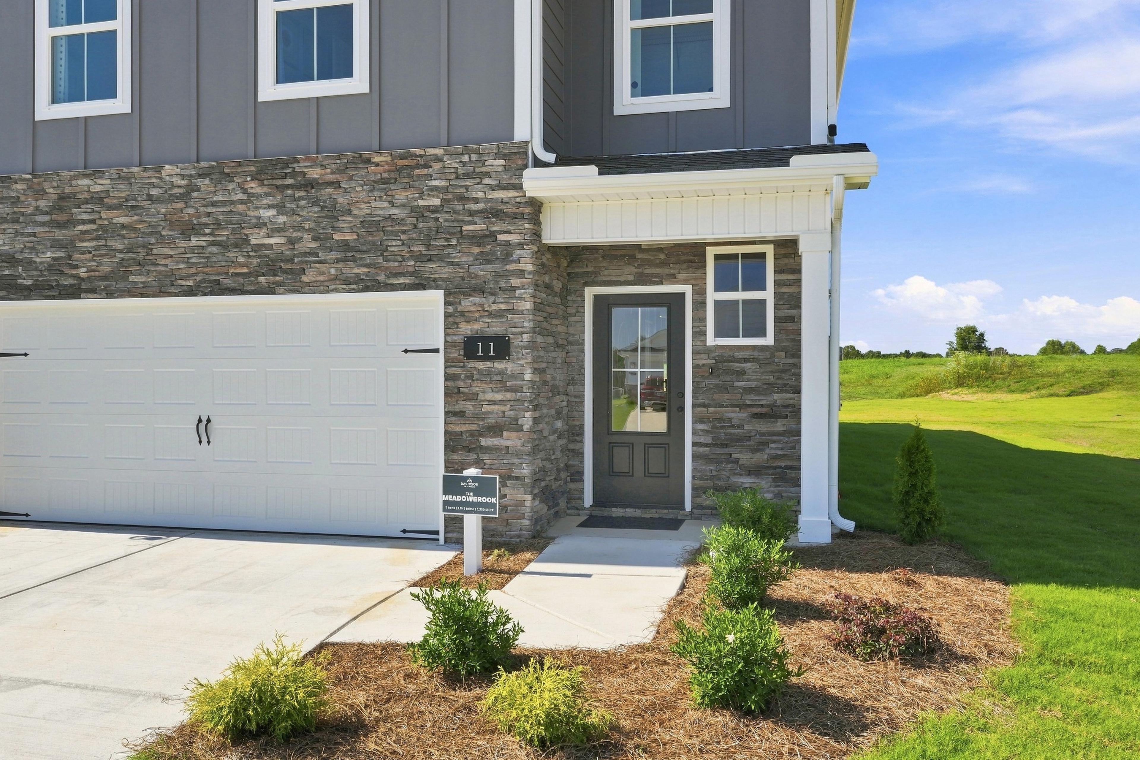 Two-story gray and stone new home exterior at Bailey Park in Fayetteville, TN by Davidson Homes with covered front porch and two-car garage