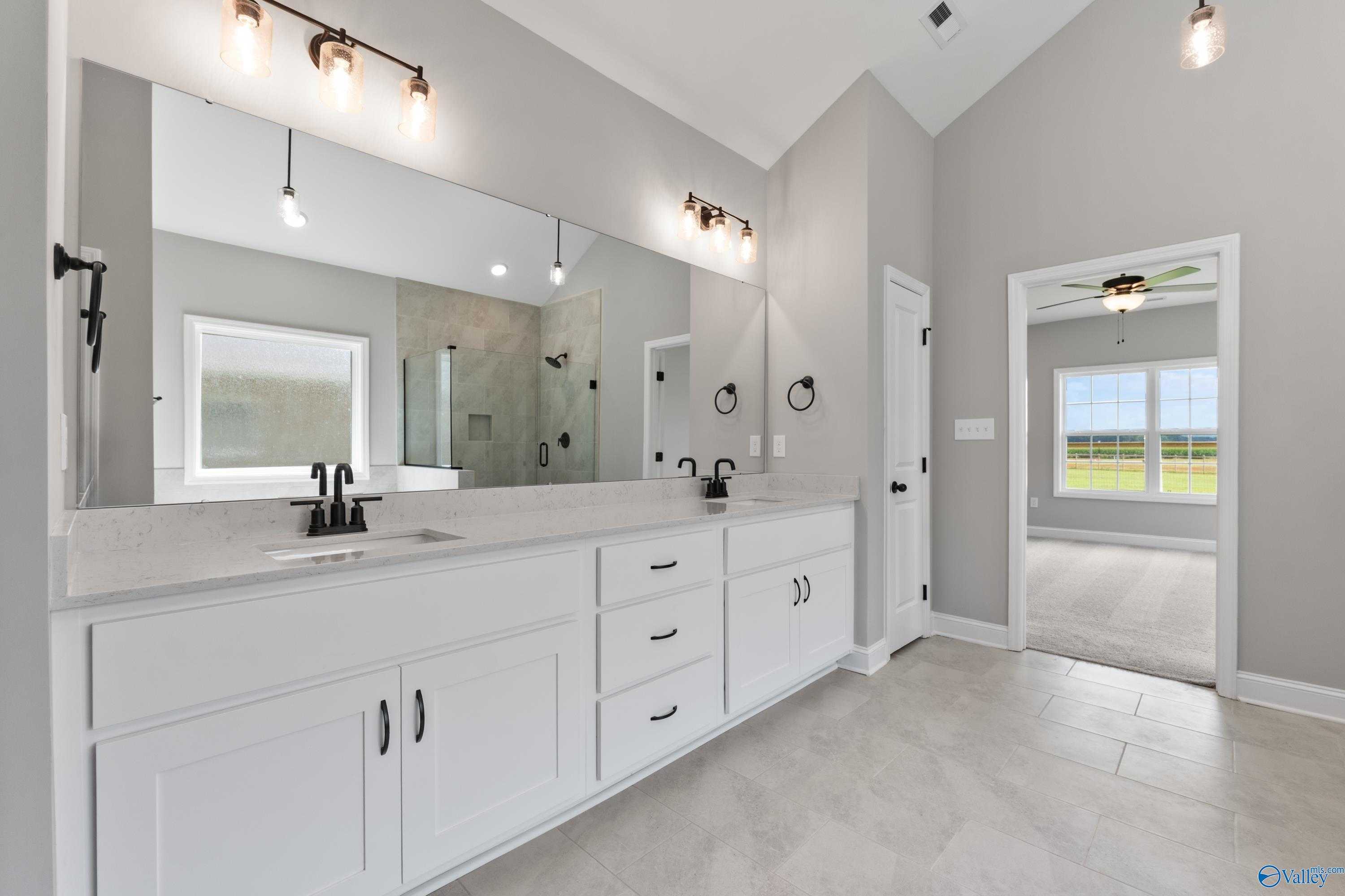 Modern master bathroom featuring double white vanity, large mirror, glass shower, and neutral gray tones in Davidson Homes The Finleigh, Toney, Alabama