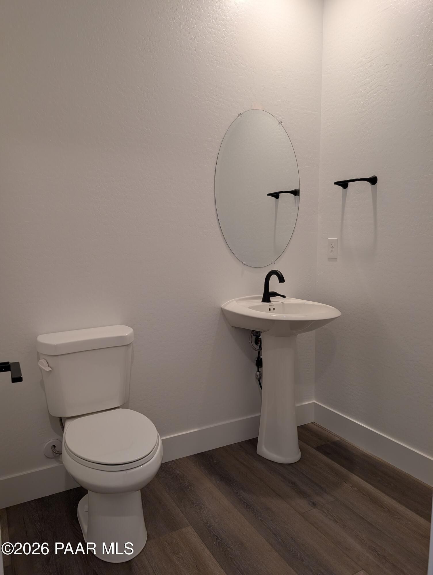 Modern powder room with round mirror, pedestal sink, white toilet, and luxury vinyl plank flooring in Davidson Homes The Sheridan II G, Prescott Arizona