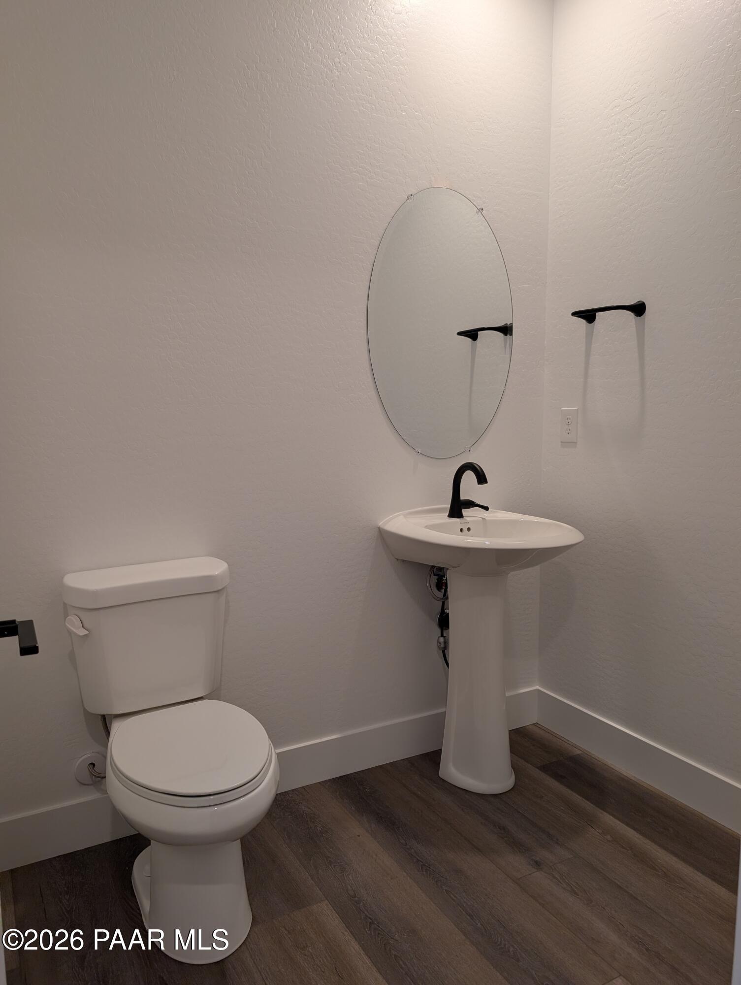 Modern powder room with round mirror, pedestal sink, white toilet, and luxury vinyl plank flooring in Davidson Homes The Sheridan II G, Prescott Arizona