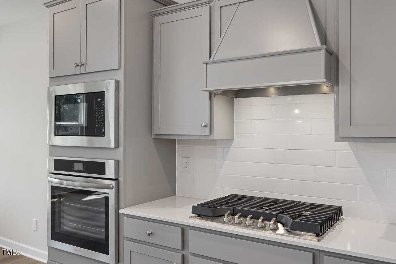 Modern gray shaker kitchen with stainless double oven, gas cooktop, white subway backsplash in Davidson Homes The Graham, Fuquay-Varina, NC