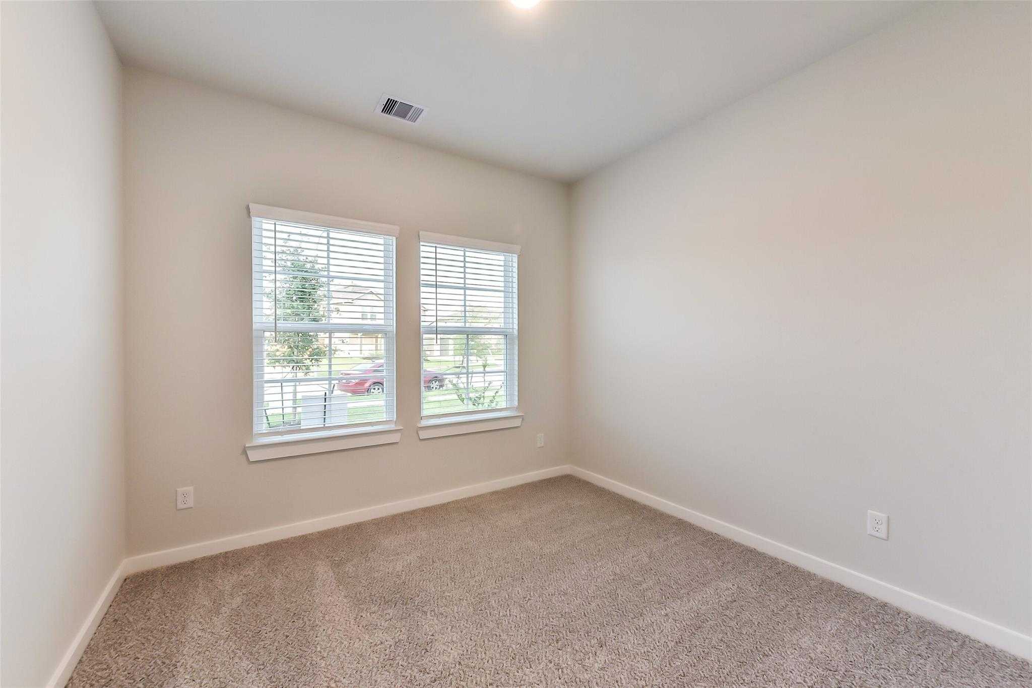 Bright secondary bedroom with neutral walls, carpet flooring, and large windows in Davidson Homes The Laguna B, Sunterra, Katy, Texas